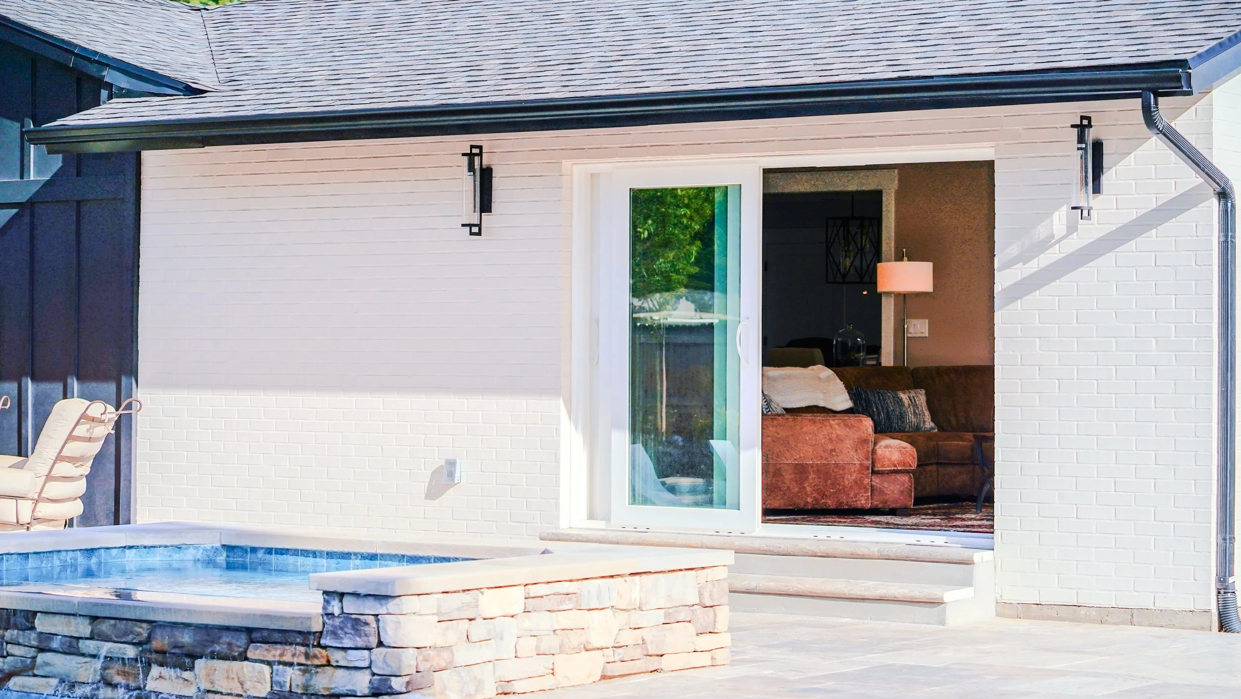 Sliding glass door with access to the backyard living space and pool, with white brick walls and lights