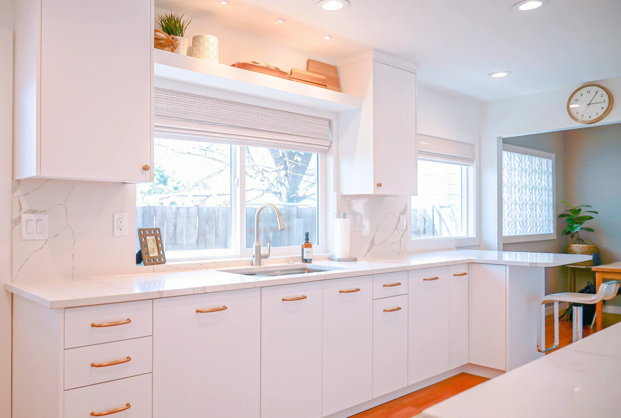 White kitchen with a window over the sink, bronze cabinet pulls, and an overhead display shelf.