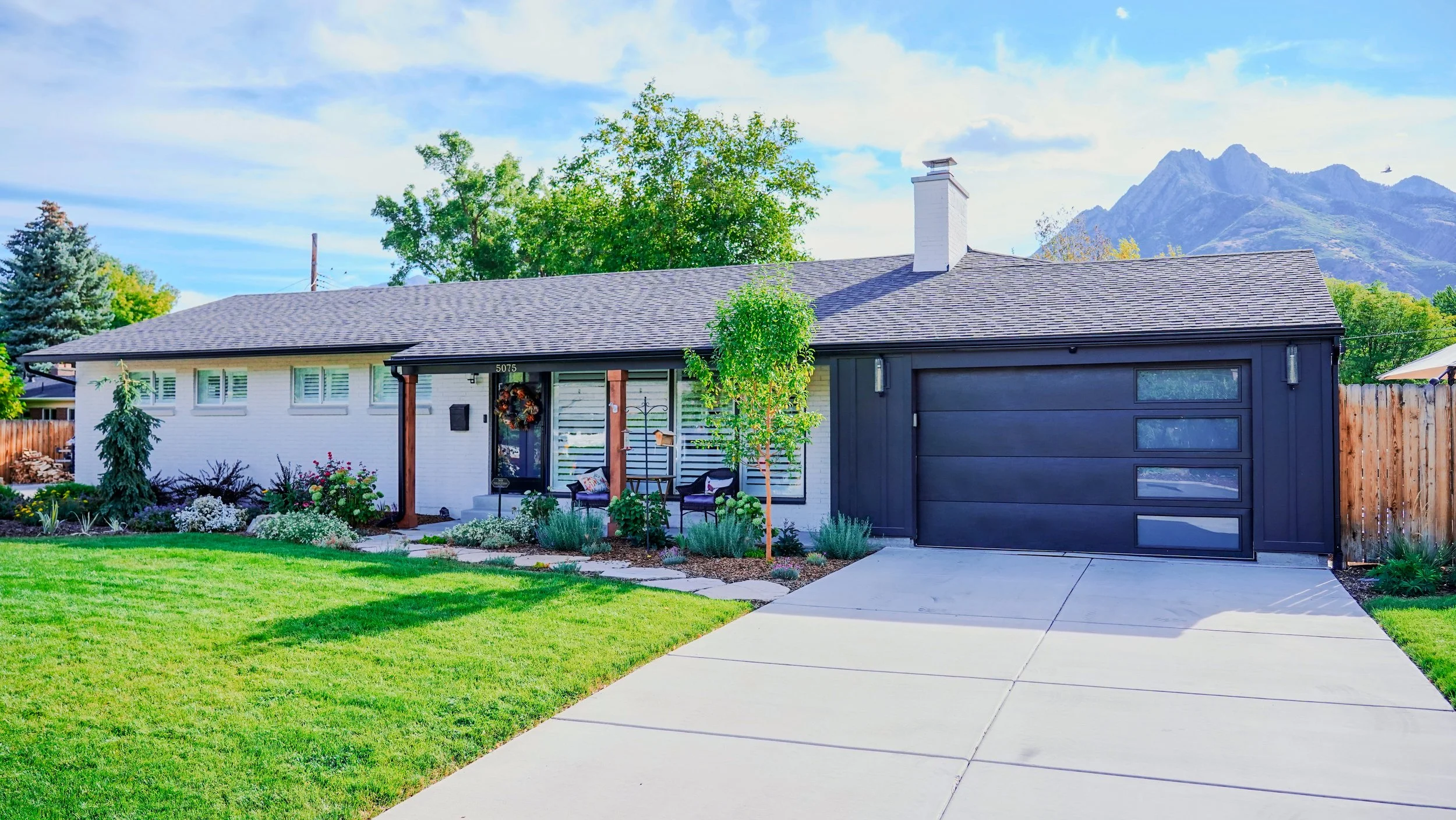 Exterior of midcentury modern house with white brick and black siding and garage with the mountains in the background