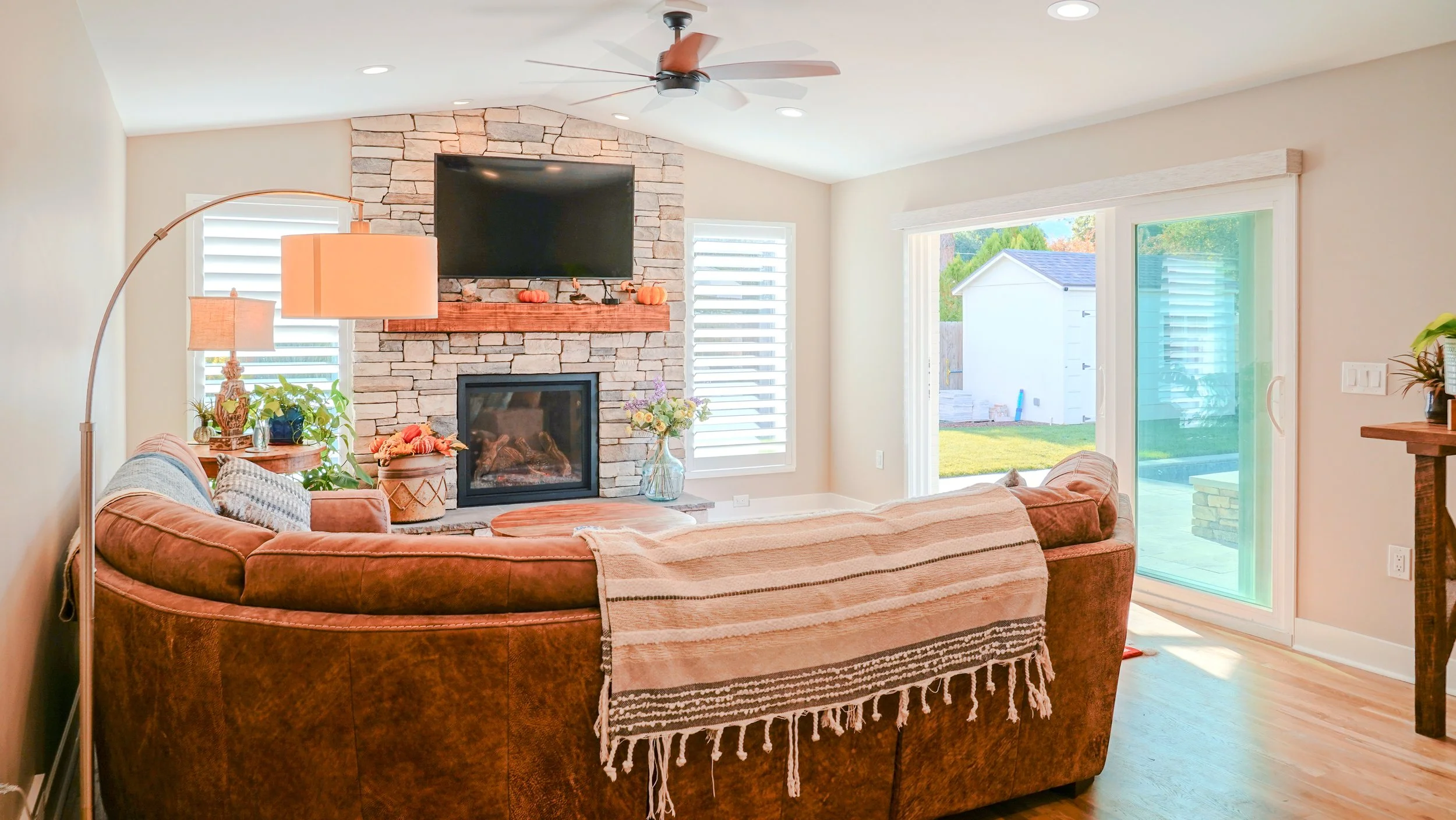 Living room with a fireplace and tv over the mantle, with sliding glass door to backyard living space