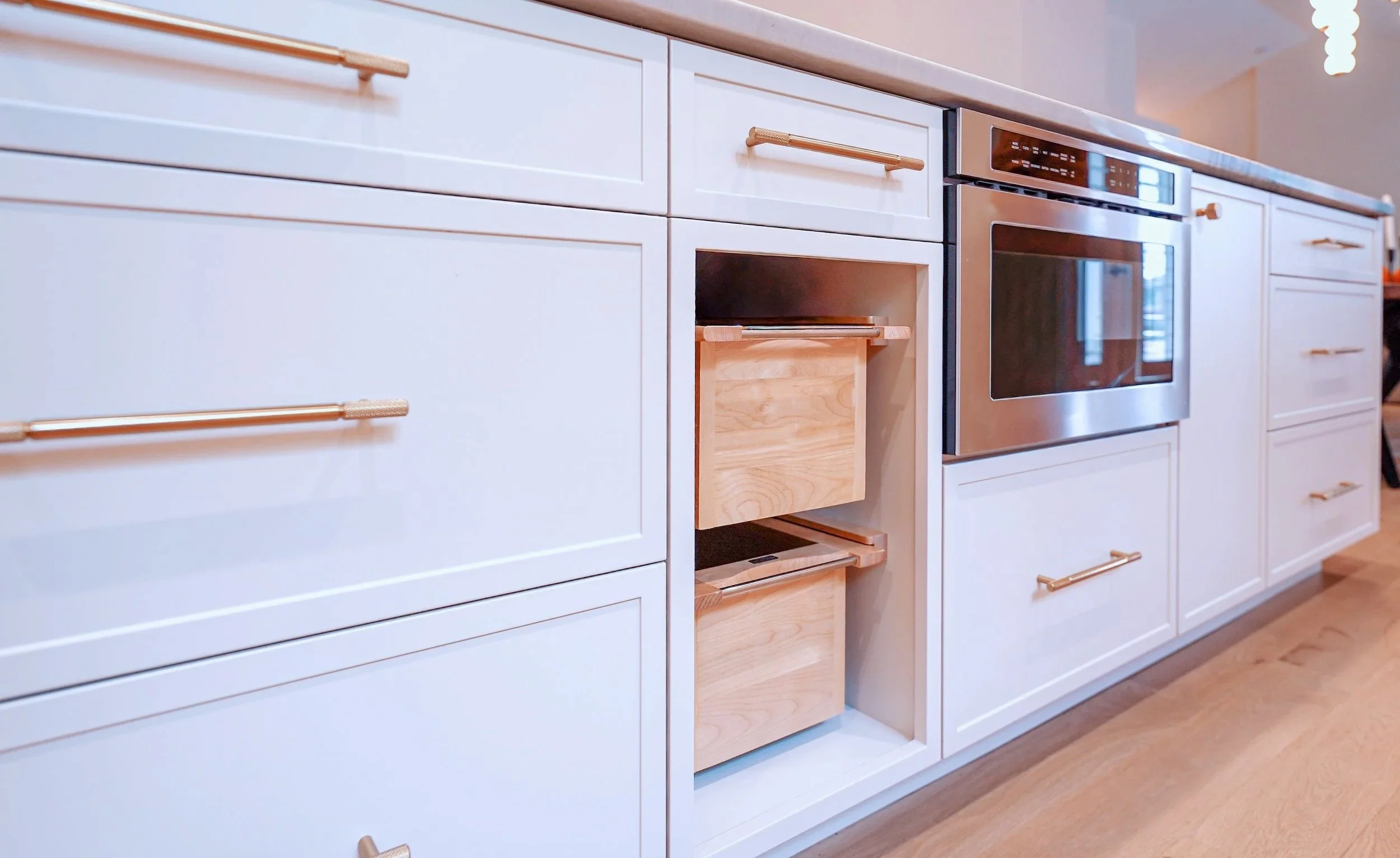 Modern kitchen with white cabinetry, stainless steel appliances, a kitchen island with a microwave, and a living room area with a sofa visible in the background.