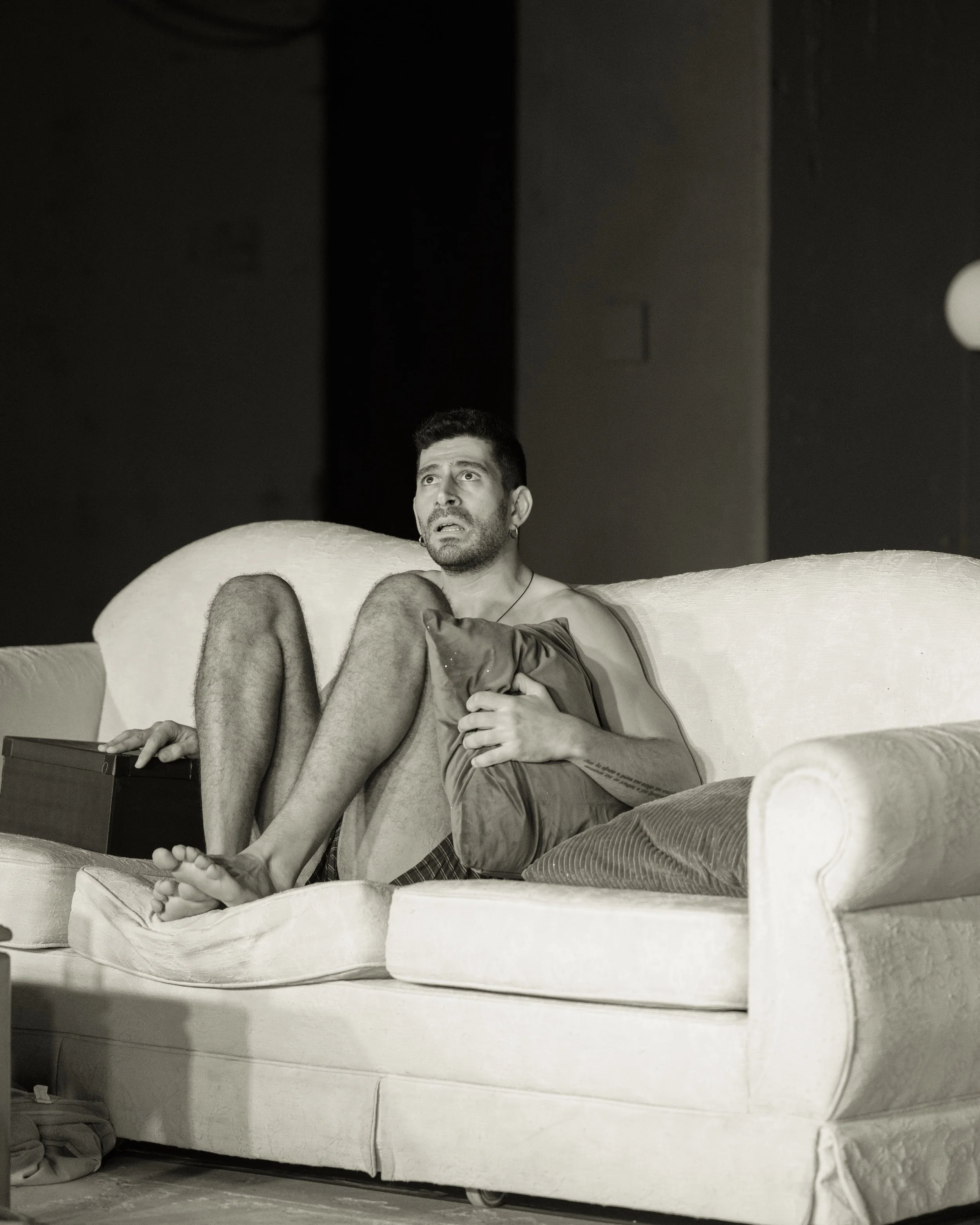 A man sitting on a couch holding a woman in his lap, both looking distressed or scared, in a black and white photo.