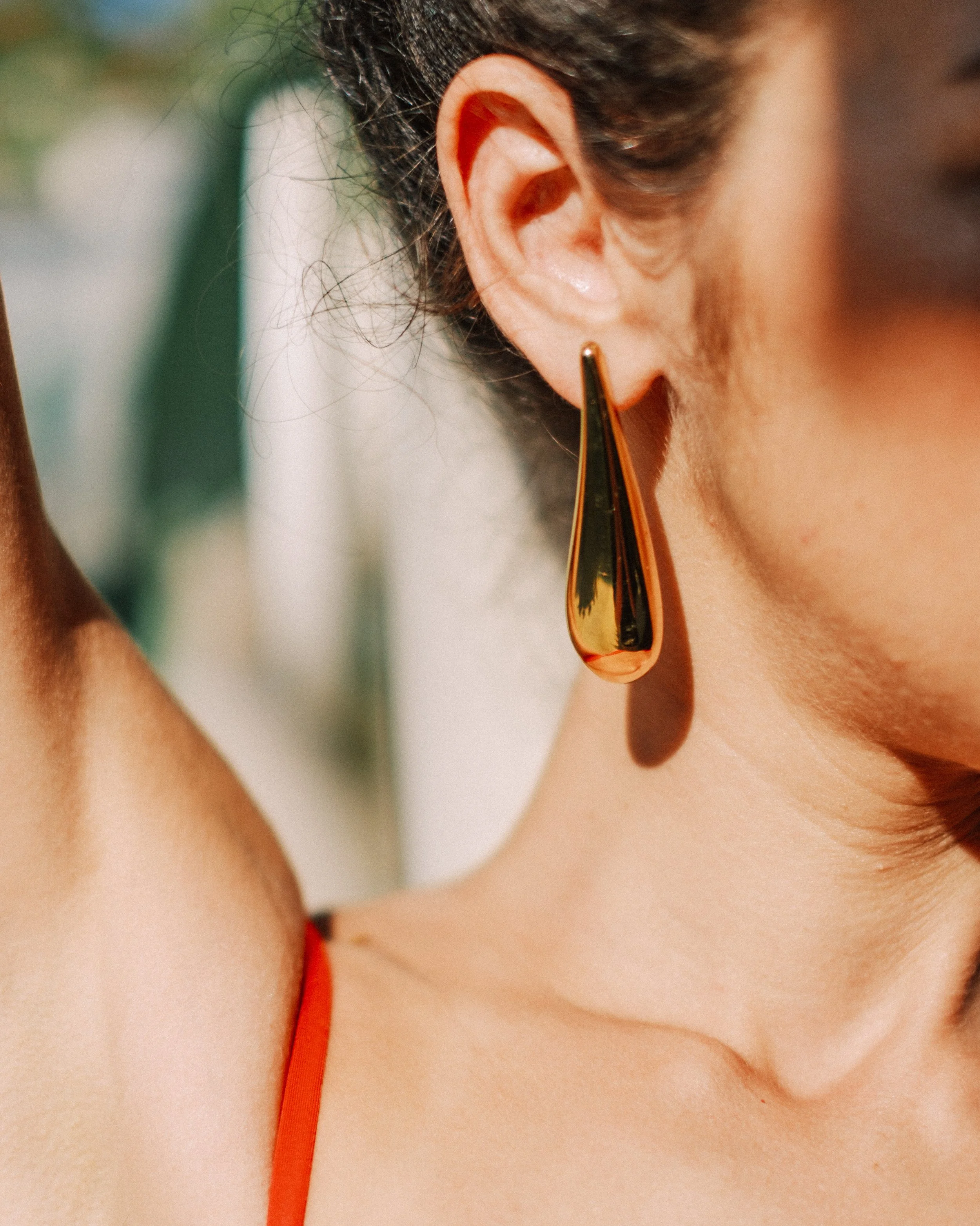 Close-up of a woman's ear wearing a large, gold teardrop-shaped earring, with her skin and shoulder visible.