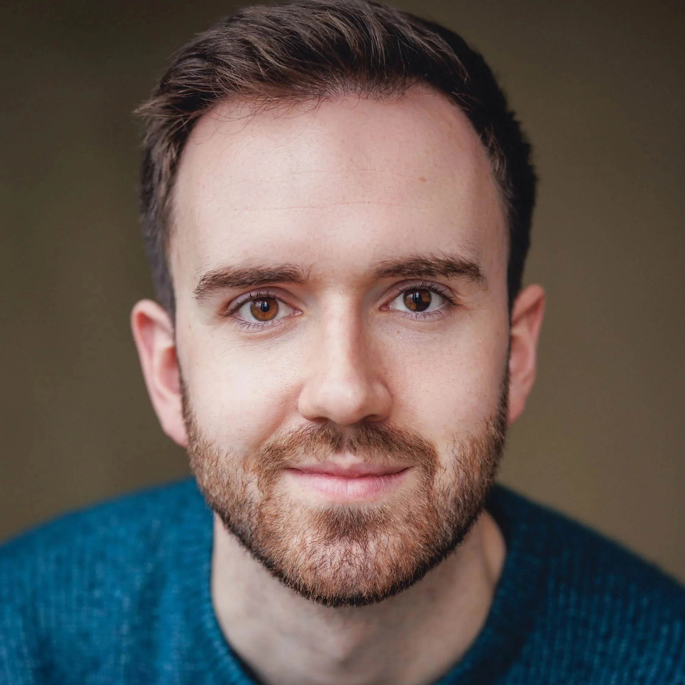 Young man with brown hair and hazelnut eyes with blue jumper