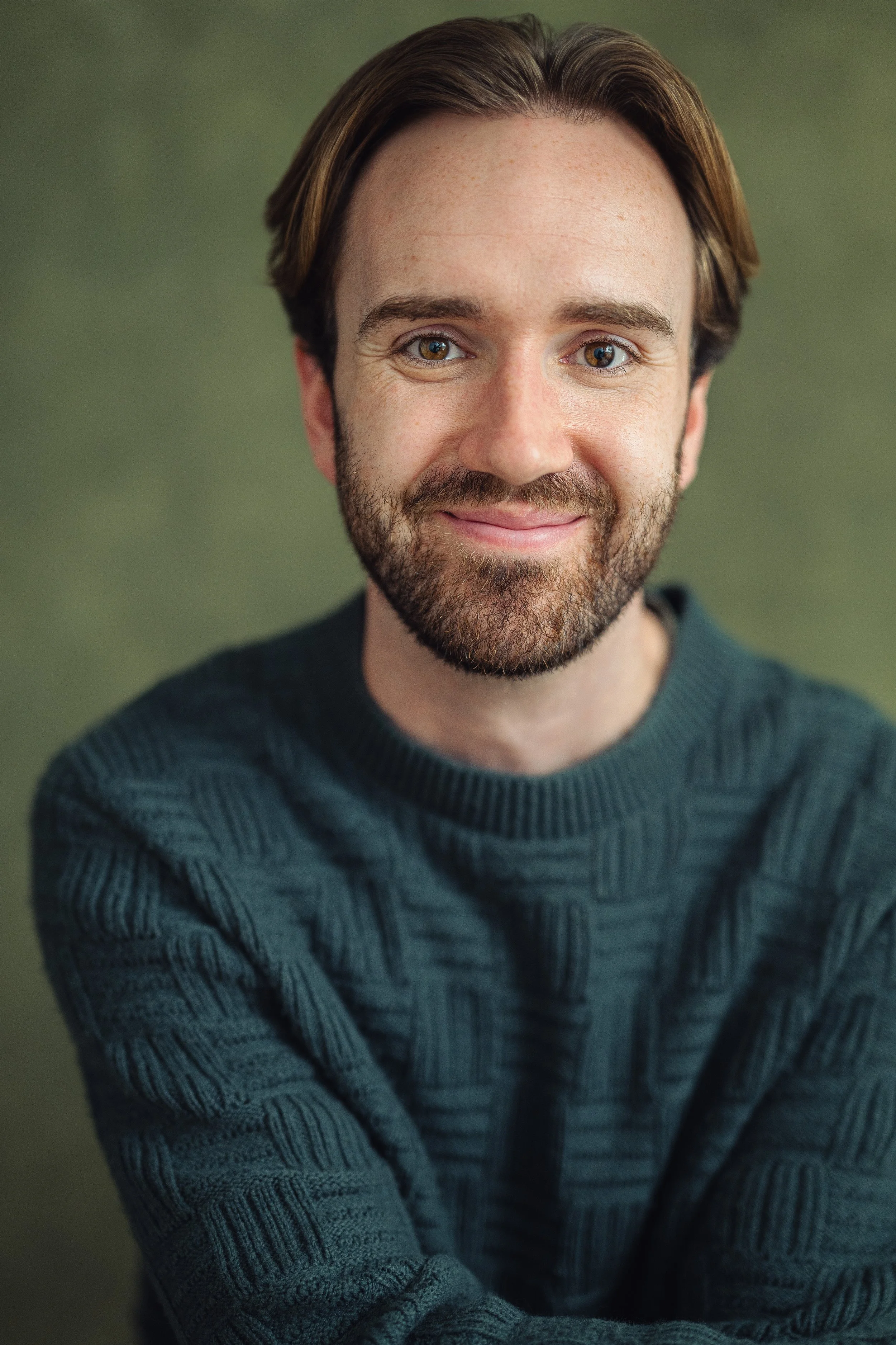 Young man with brown hair and hazelnut eyes with green jumper