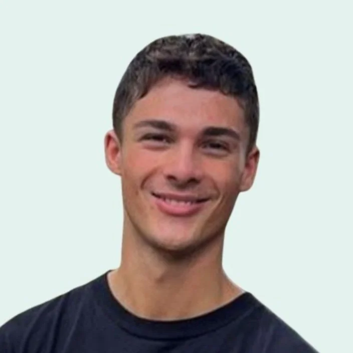A young man with short dark hair, smiling, wearing a black T-shirt, against a light background.