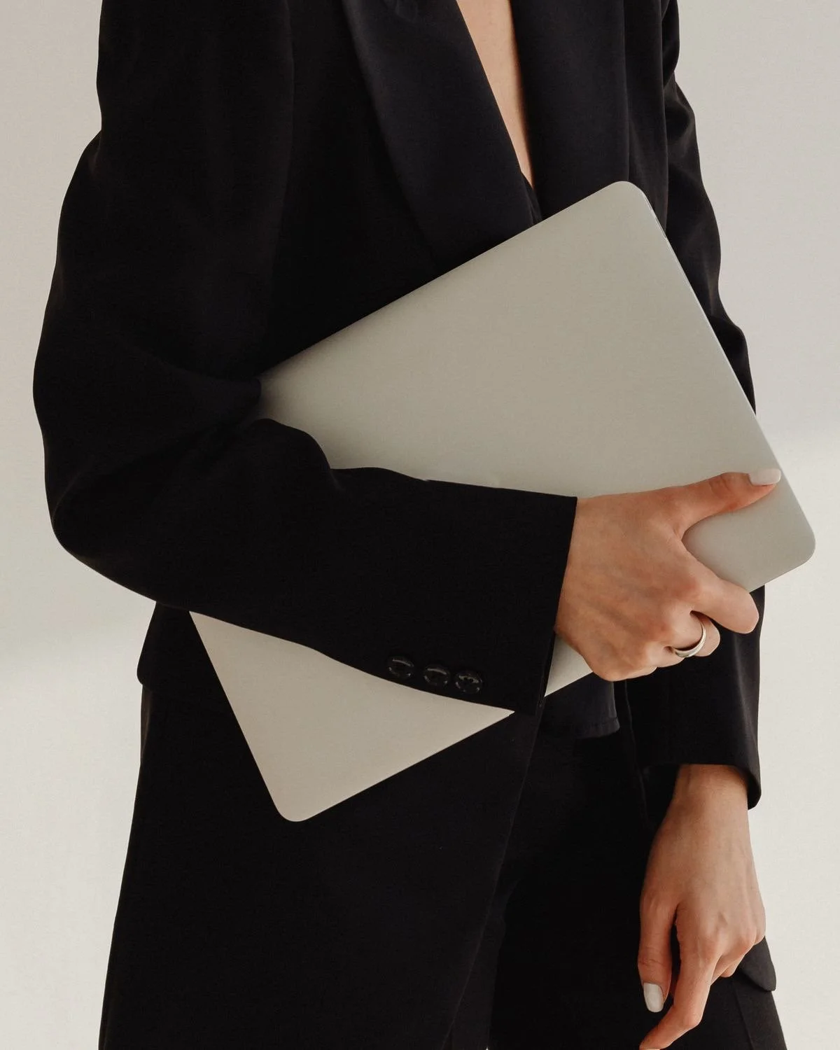 Person in black suit holding a closed laptop.