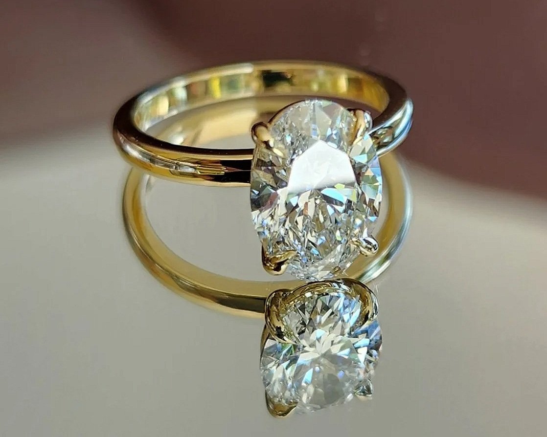 A 18ctyellow gold engagement ring with a large 2ct oval diamond, placed on a reflective surface.