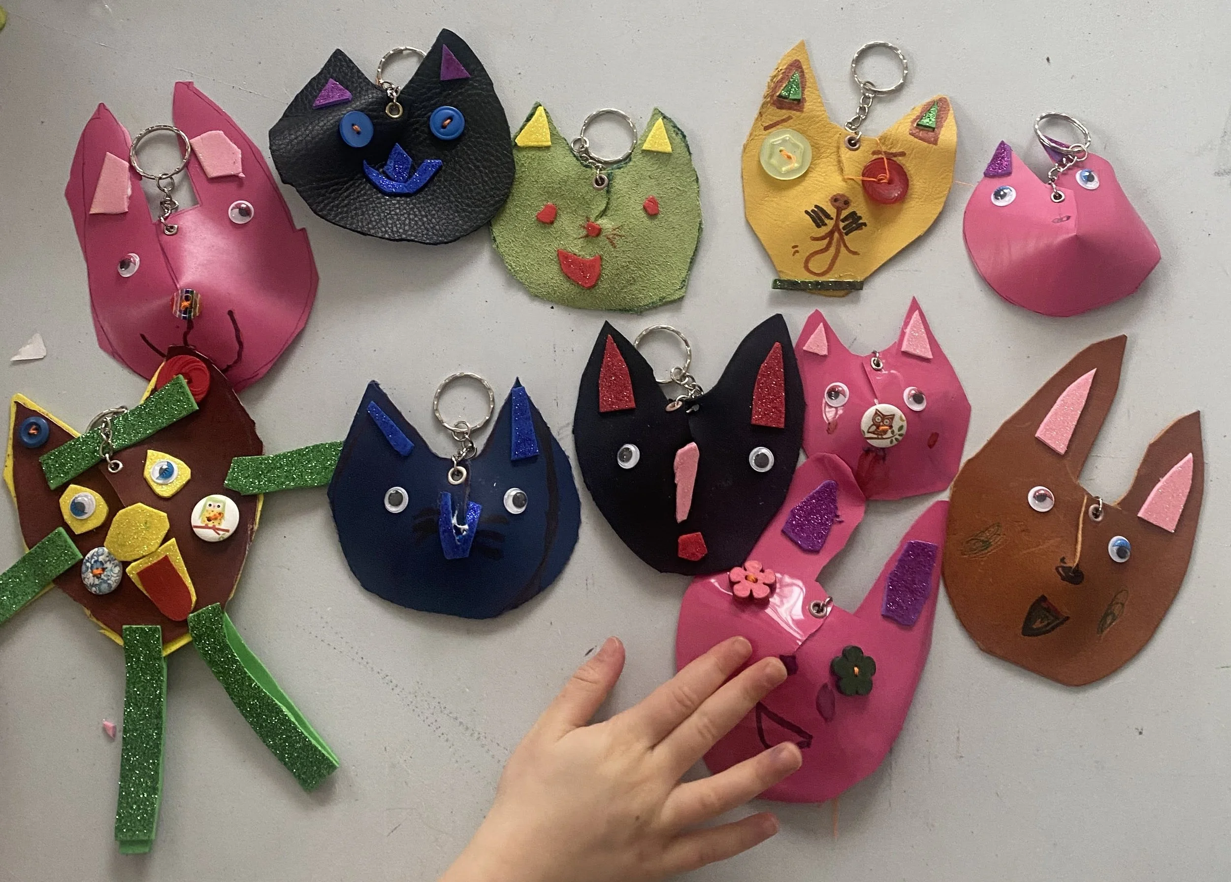 Various handmade animal face keychains with a cat, dog, and bear design on a green background with orange lines.