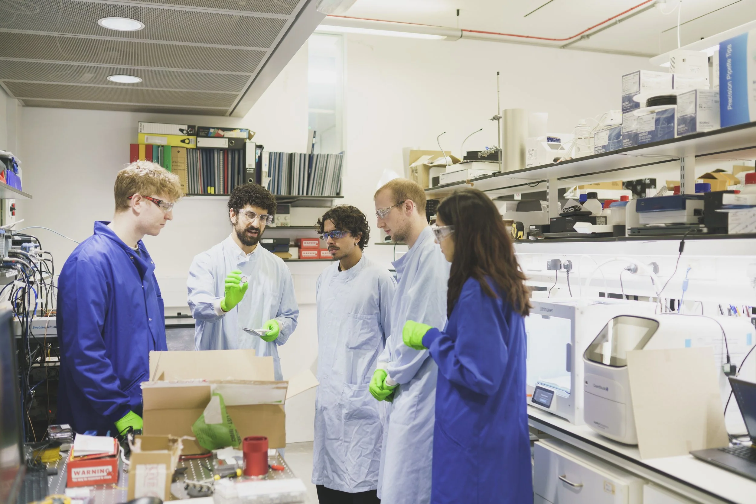 five people in lab coats looking at an object in the lab