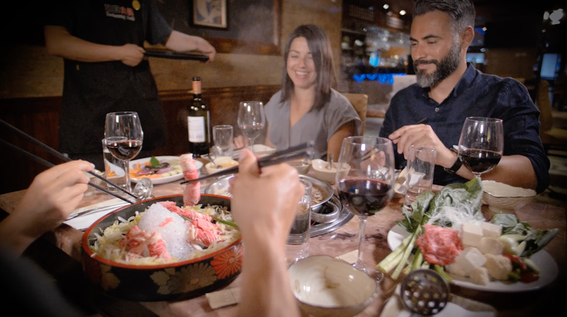 Group enjoying a meal at a restaurant with hot pot, wine, and various dishes on the table.