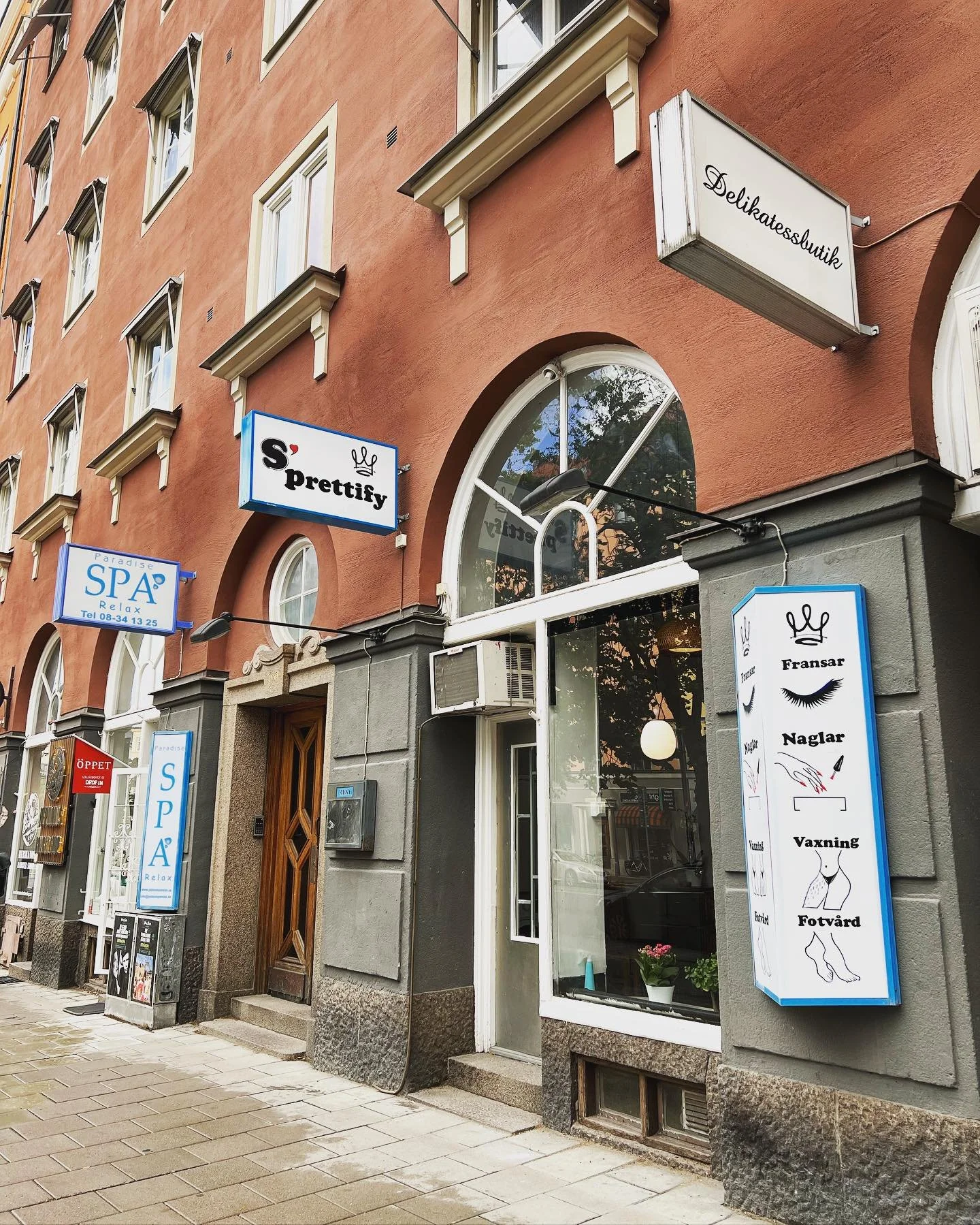 Street view of a building with a spa and beauty salon called S'prettify, featuring signs for beauty services like eyelash extensions and nail care, along with a delicatessen sign.