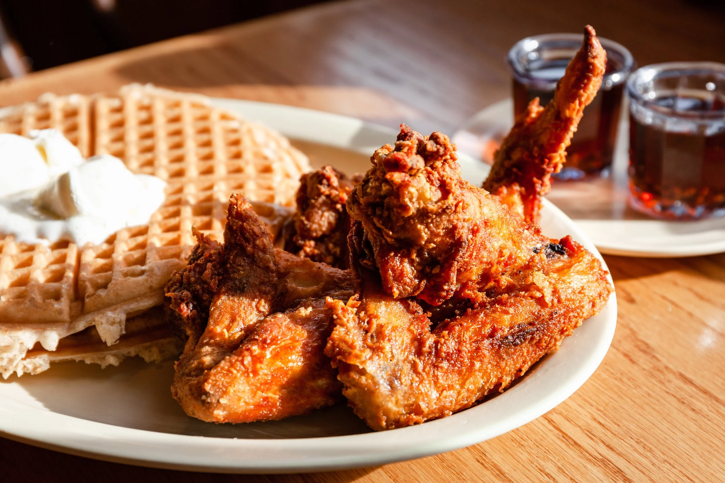 Plate of chicken and waffles with syrup on a wooden table.