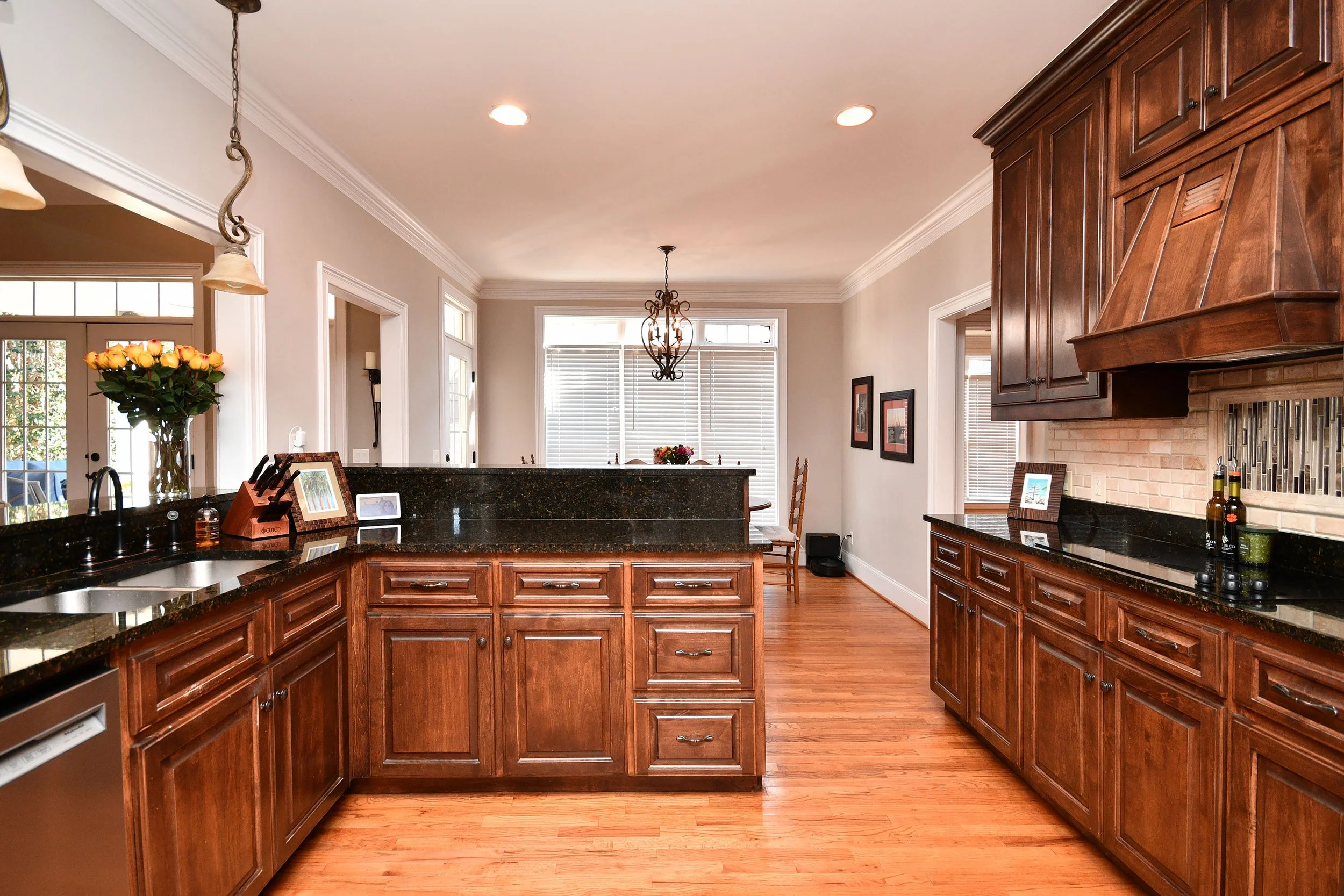 Kitchen with wooden cabinets, black granite countertops, and hardwood floor, with a dining area and large windows in the background. Home for sale in Greenville, SC. Master on Main Level. 4 Bedroom home for sale. Upscale Community. 