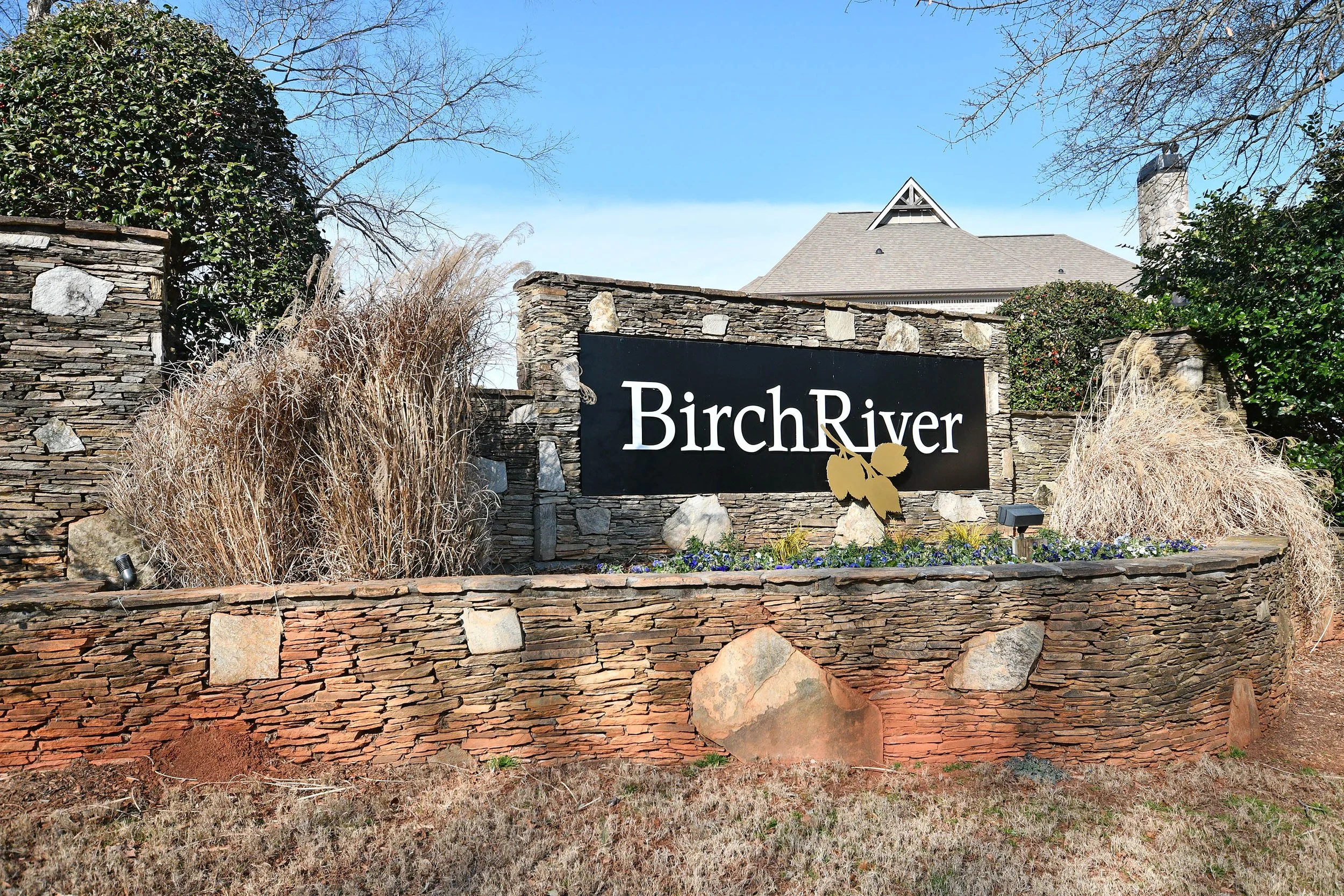 Entrance sign for Birch River with stone and brick landscaping, decorative plants, and a house in the background. Home for sale in Greenville, SC. Master on Main Level. 4 Bedroom home for sale. Upscale Community. 