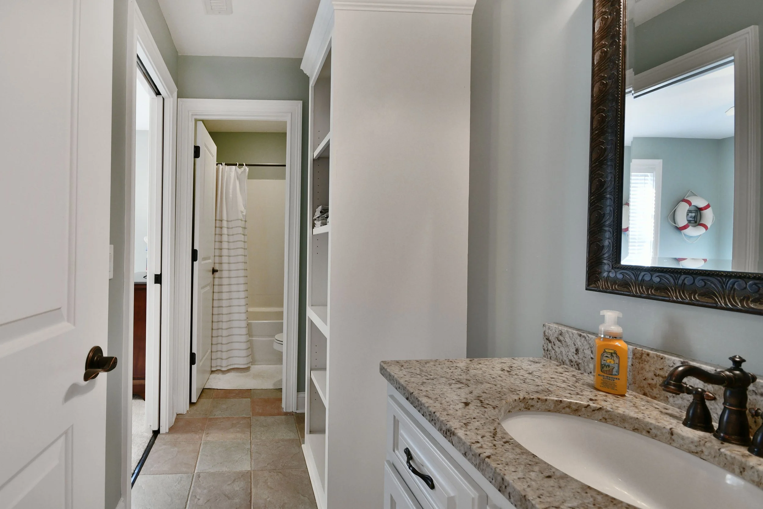 Bathroom with granite countertop, mirror, sink, soap dispenser, open shelves, and a view of a shower with striped curtain and bathtub in background. Home for sale in Greenville, SC. Master on Main Level. 4 Bedroom home for sale. Upscale Community. 