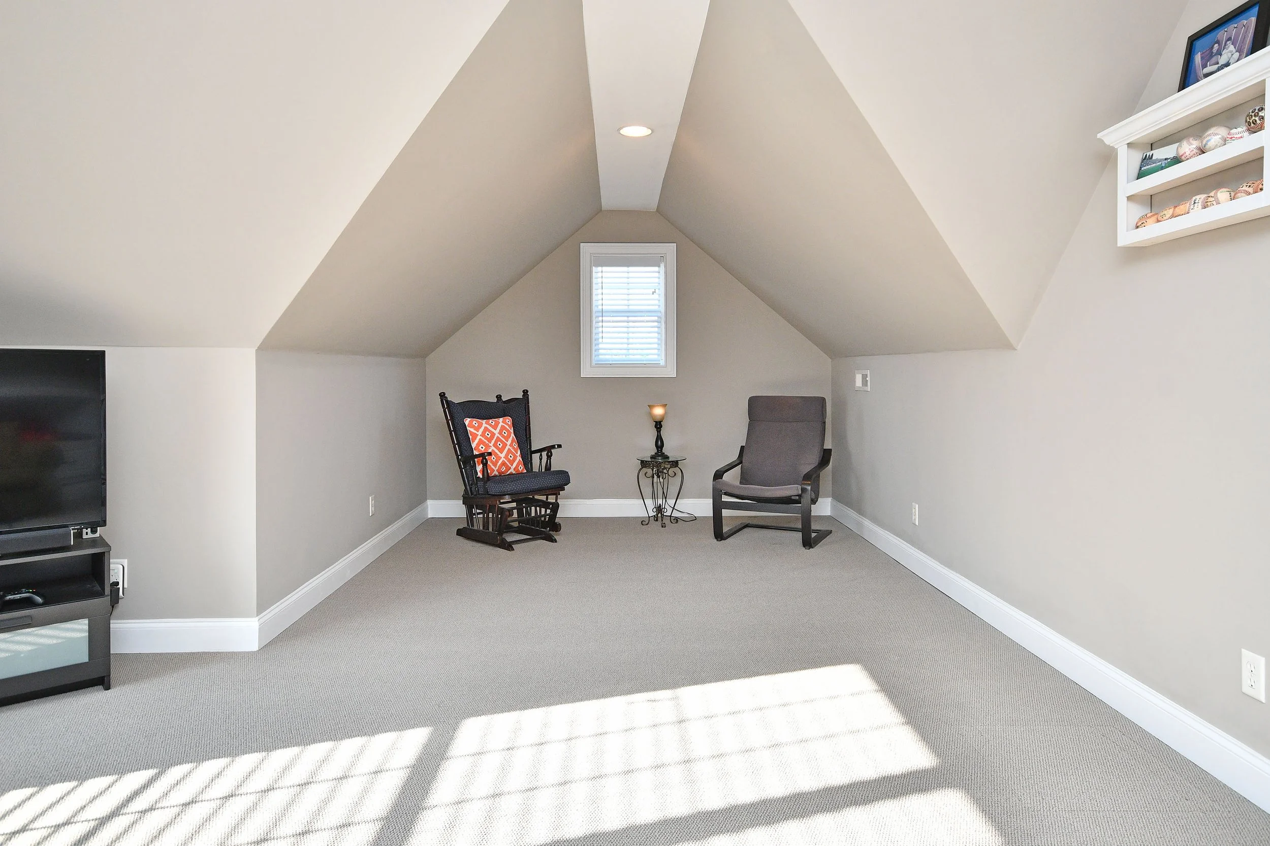 Empty attic room with sloped ceiling, small window, beige carpet, two chairs, small side table with candle, and framed picture on wall. Home for sale in Greenville, SC. Master on Main Level. 4 Bedroom home for sale. Upscale Community. 