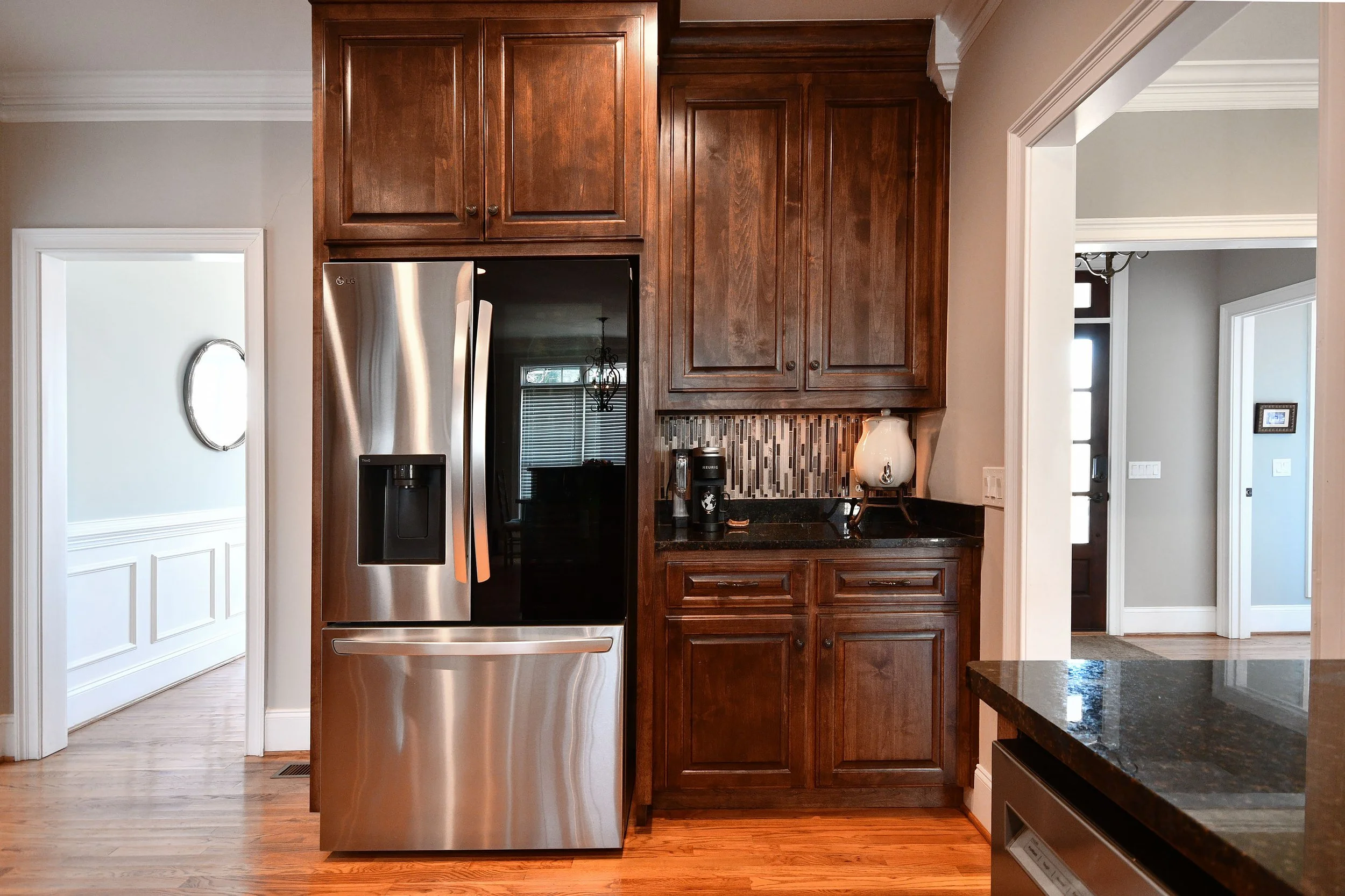 Kitchen with stainless steel LG refrigerator, dark wood cabinets, black granite countertop, and a small coffee station with a k-cup machine and a decorative lamp. Home for sale in Greenville, SC. Master on Main Level. 4 Bedroom home for sale. Upscale