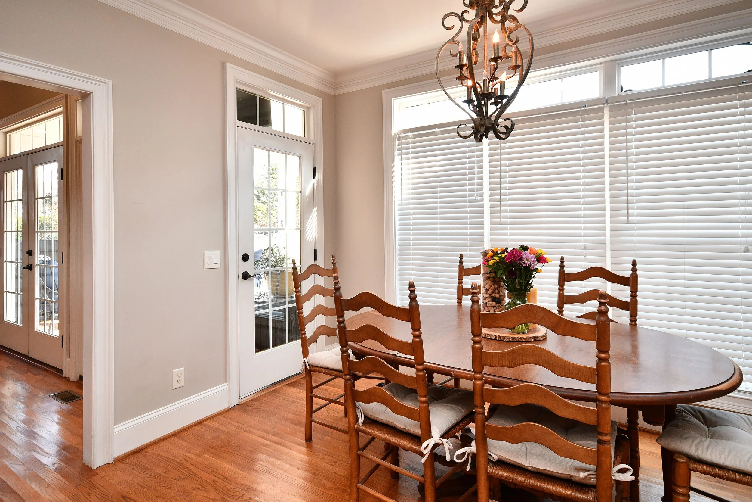 Dining room with a wooden table and chairs, a floral centerpiece, large windows with blinds, a chandelier, and a glass door leading outside. Home for sale in Greenville, SC. Master on Main Level. 4 Bedroom home for sale. Upscale Community. 