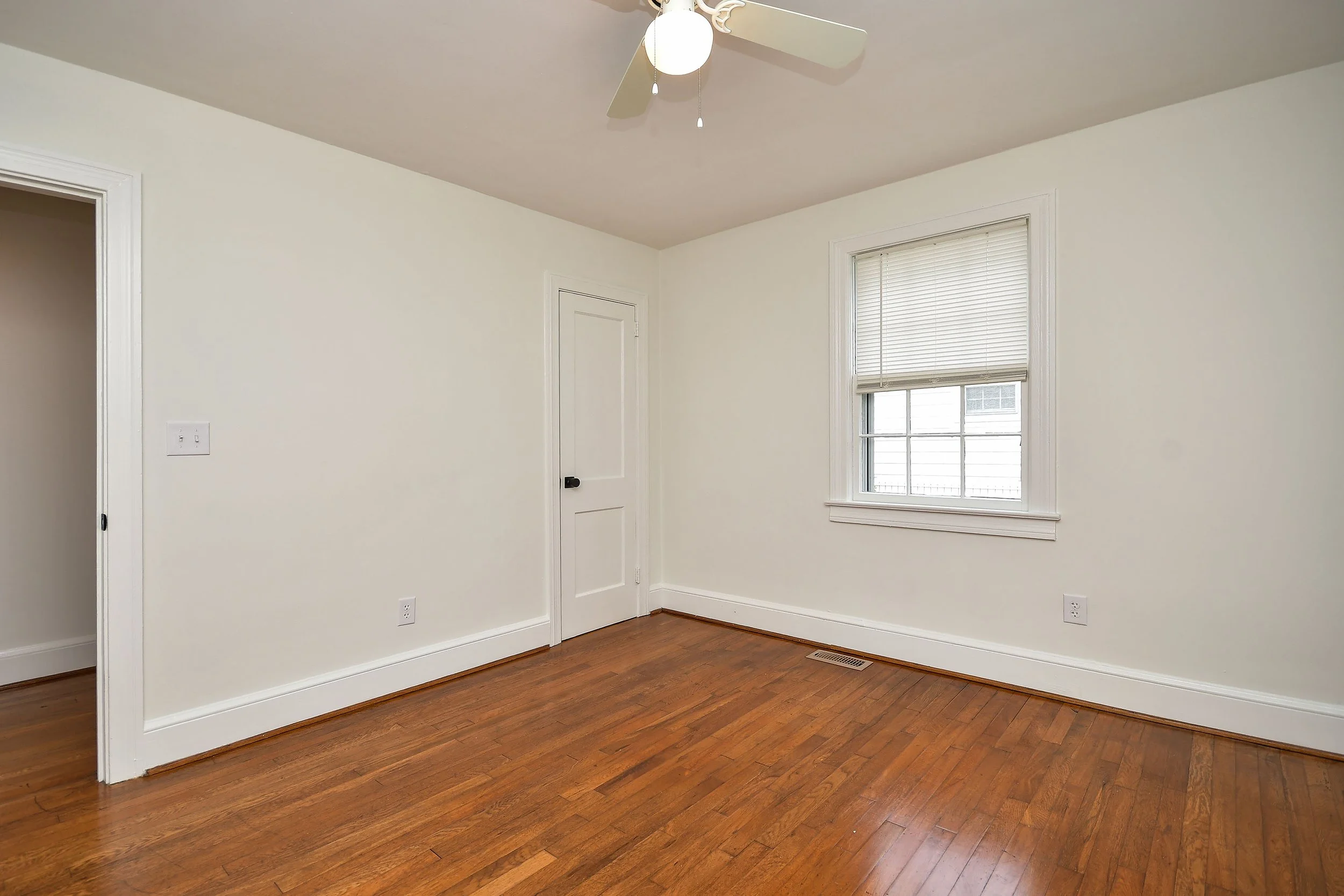 Empty room with white walls, hardwood floor, a window with blinds, and a ceiling fan with lights.