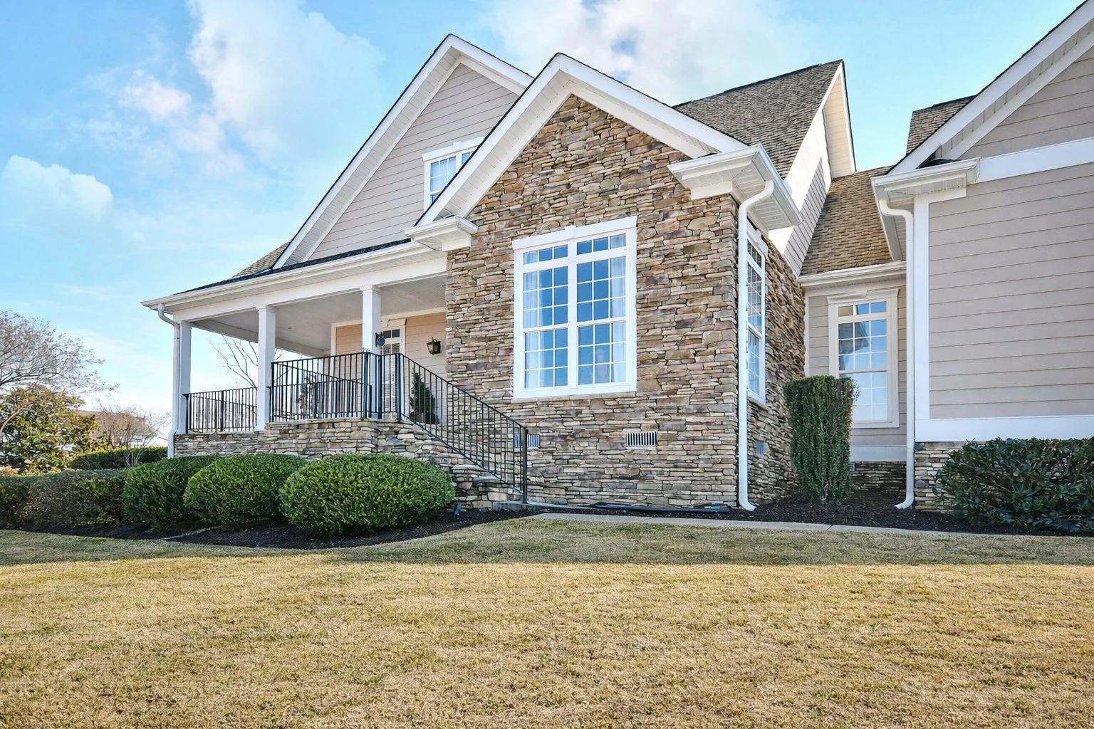 A modern house features a stone and siding exterior, large windows, a front porch with black railing, and a well-manicured lawn. Home for sale in Greenville, SC. Master on Main Level. 4 Bedroom home for sale. Upscale Community. 