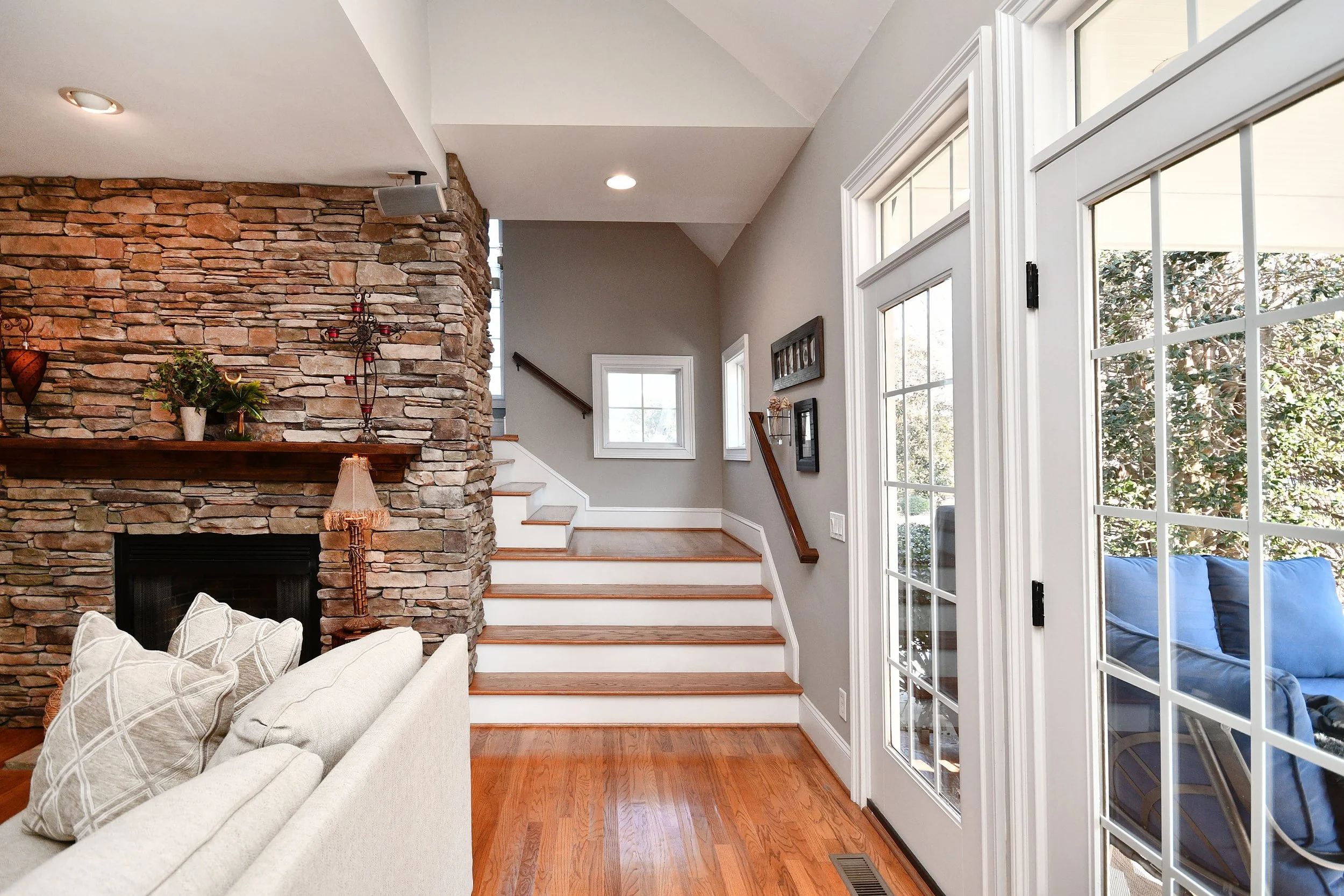Living room with stone fireplace, beige sofa, hardwood floor, staircase, and large glass doors leading outside. Home for sale in Greenville, SC. Master on Main Level. 4 Bedroom home for sale. Upscale Community. 