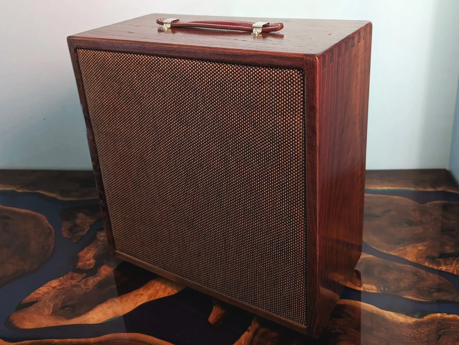 A vintage wooden portable speaker with a handle on top, placed on a wooden surface.