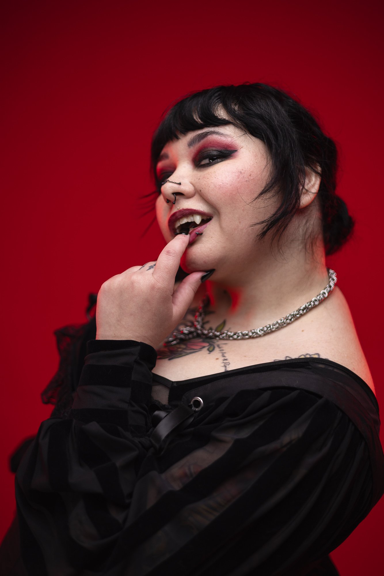 Person with vampire fangs in a black outfit against a red background.