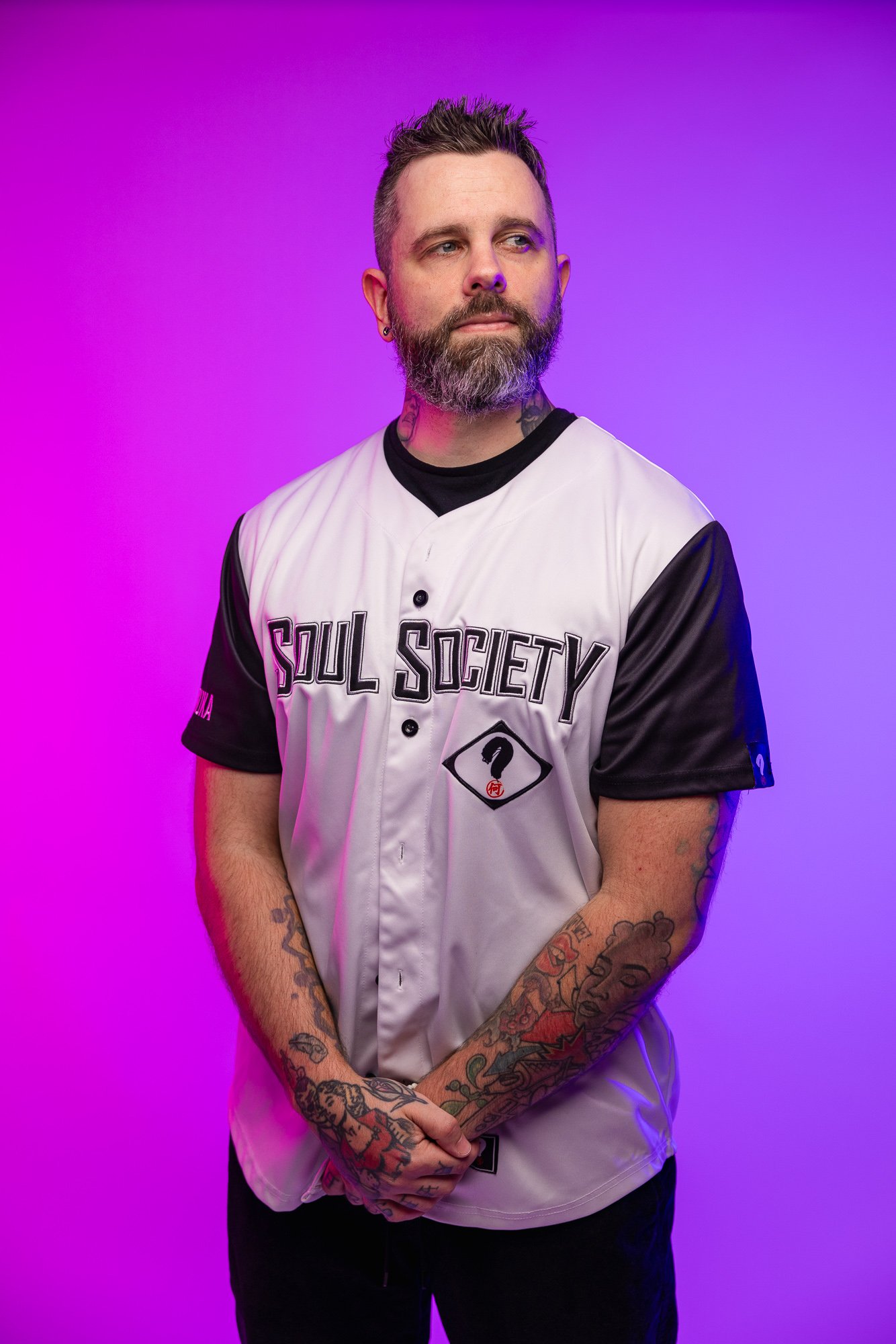 Man with tattoos wearing a 'Soul Society' jersey standing against a purple background.