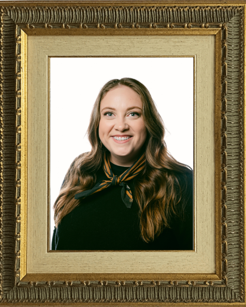Framed portrait of Devyn Steele wearing a black blouse and an orange and green scarf standing against a plain background.