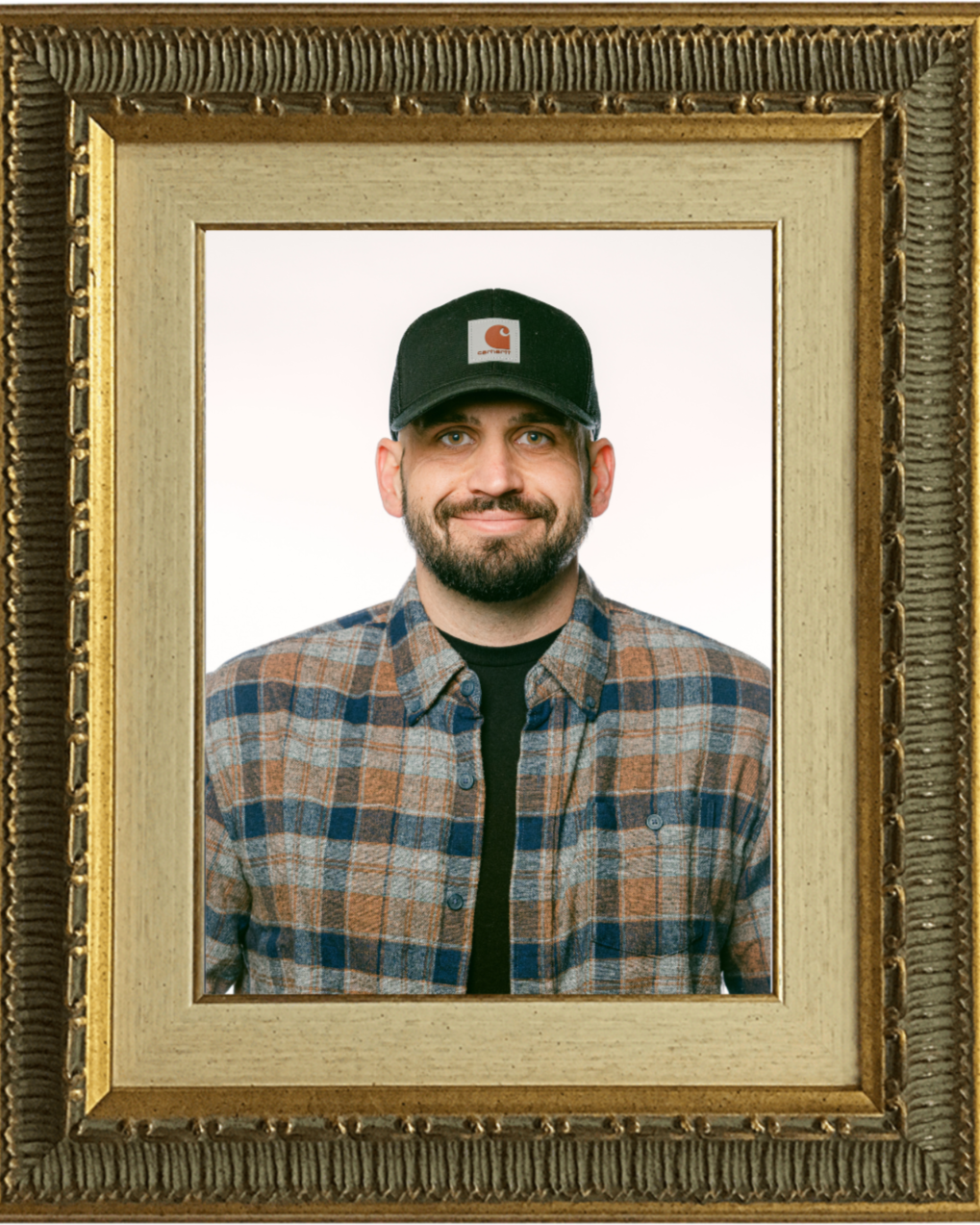 Framed portrait of Mike Johnson wearing a plaid shirt and black hat standing against a plain background.