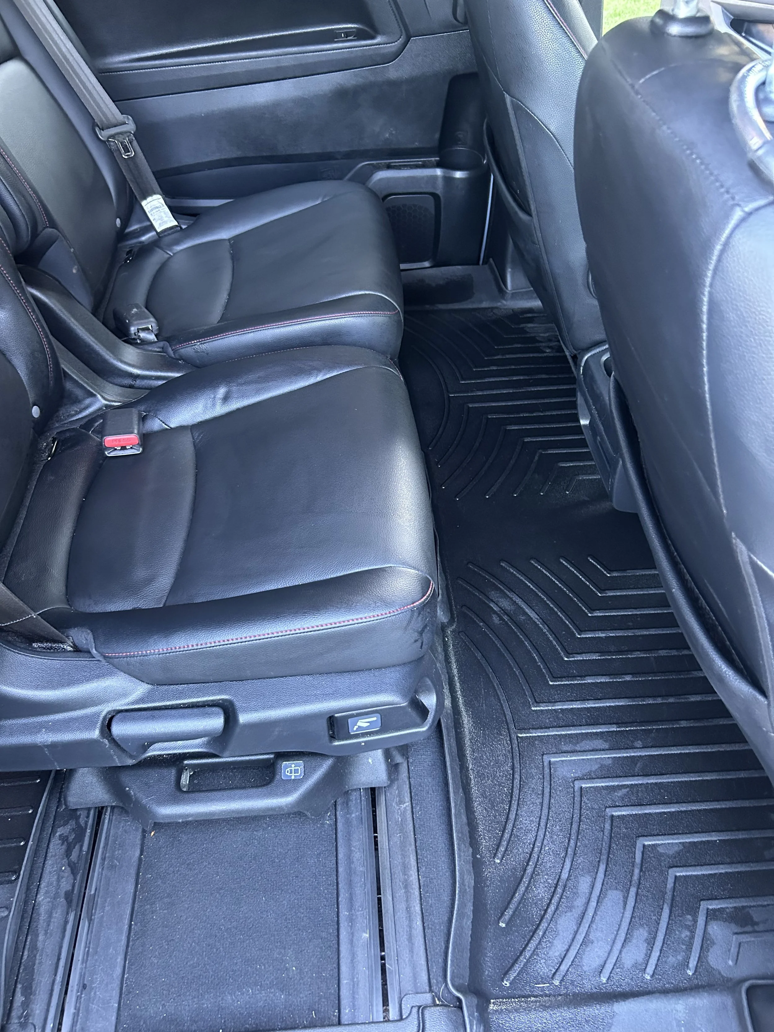 Interior of a vehicle showing black leather back seats, a rubber floor mat, and the back of the front passenger seat.