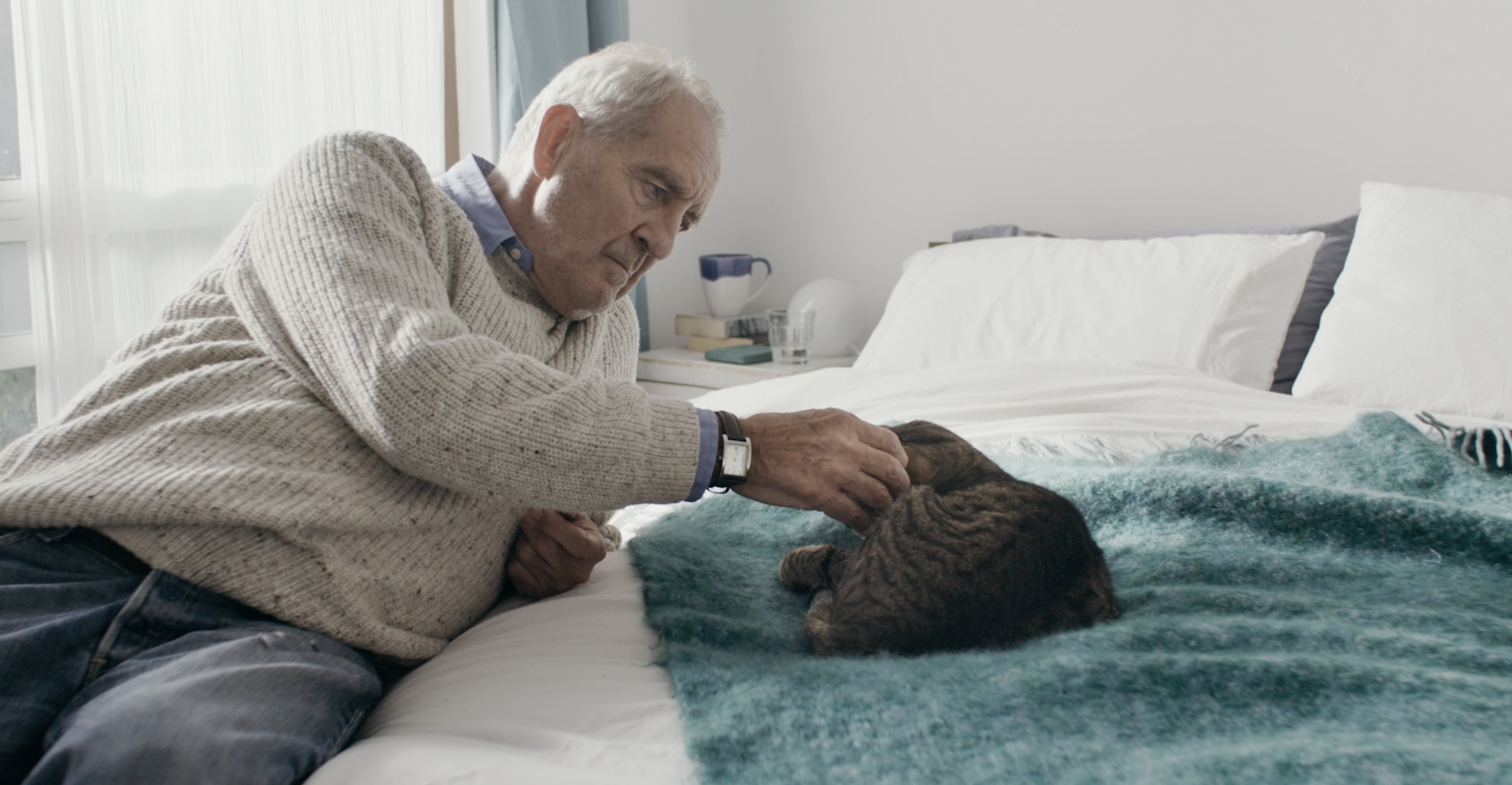 Elderly man tenderly stroking cat on bed, emotional healthcare storytelling campaign for Ferring Pharmaceuticals by STORO