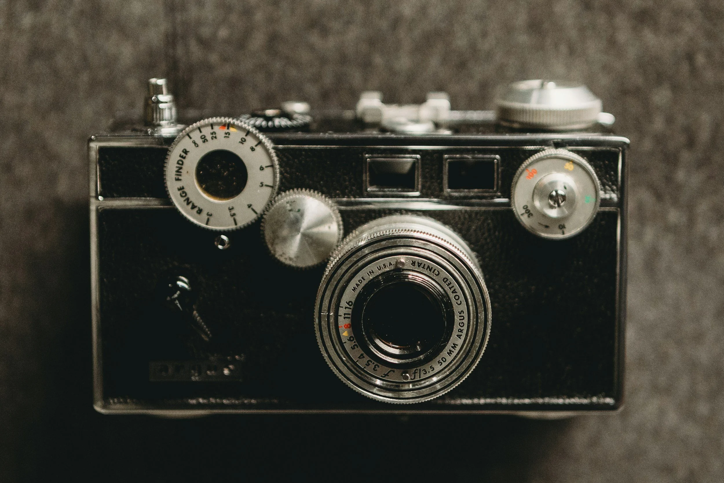 Close-up of a vintage black and silver camera with various dials and a textured body on a dark surface.