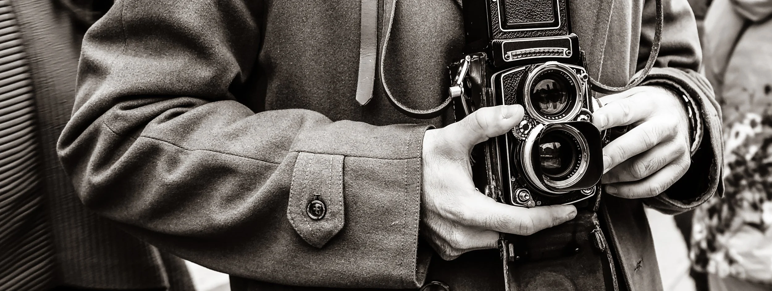 Person holding a vintage camera with both hands, wearing a long-sleeve jacket.