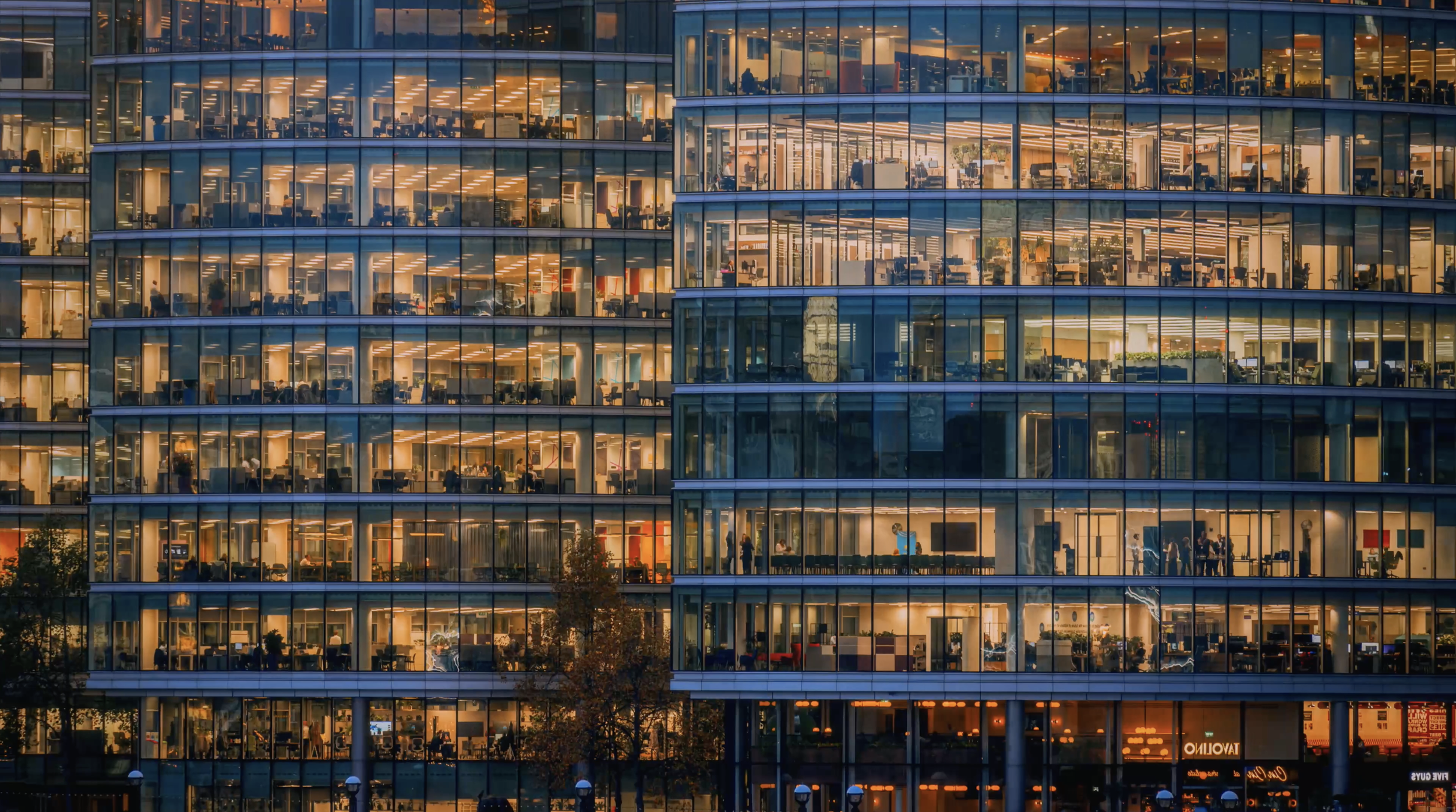 Glass-fronted office building at dusk, workers visible across multiple floors, representing the organisations STORO helps tell their story