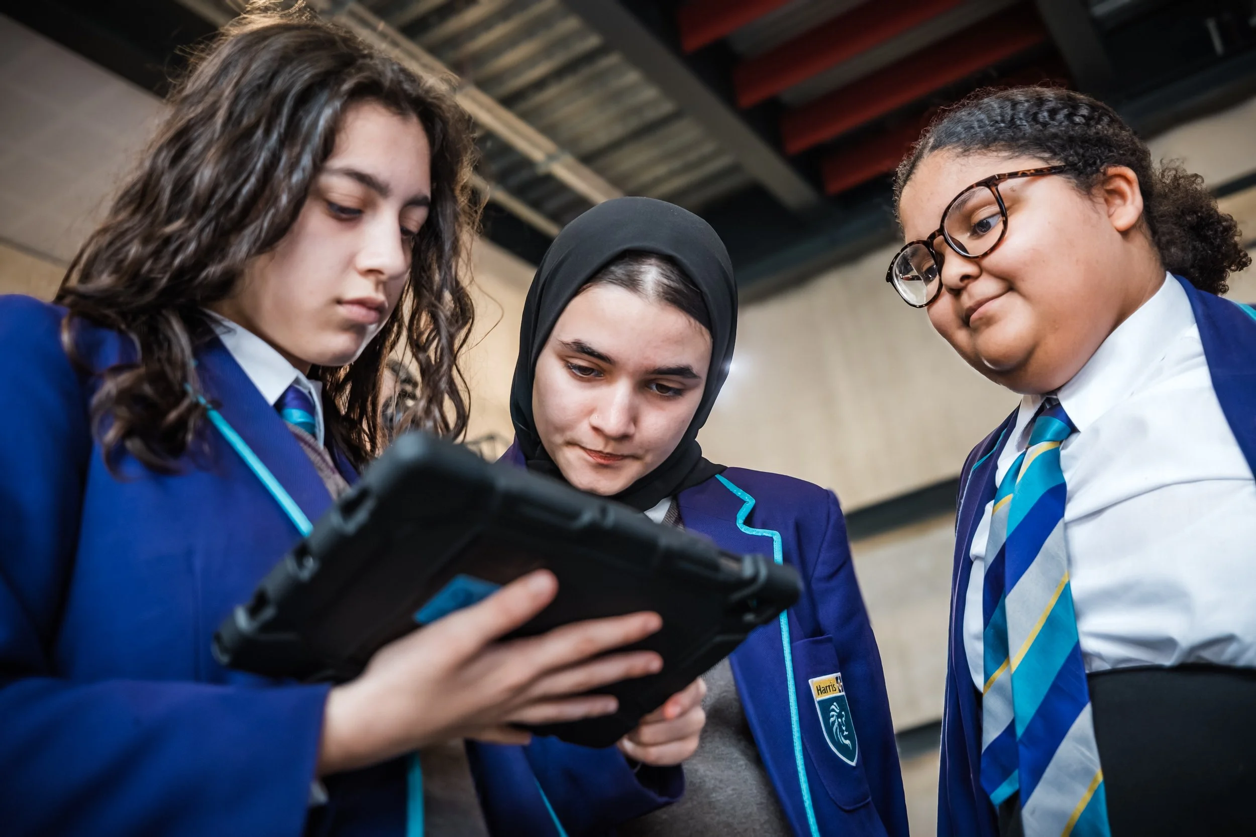 Three schoolgirls studying tablet together in uniform, sustainability and social value campaign for LetsLocalise by STORO
