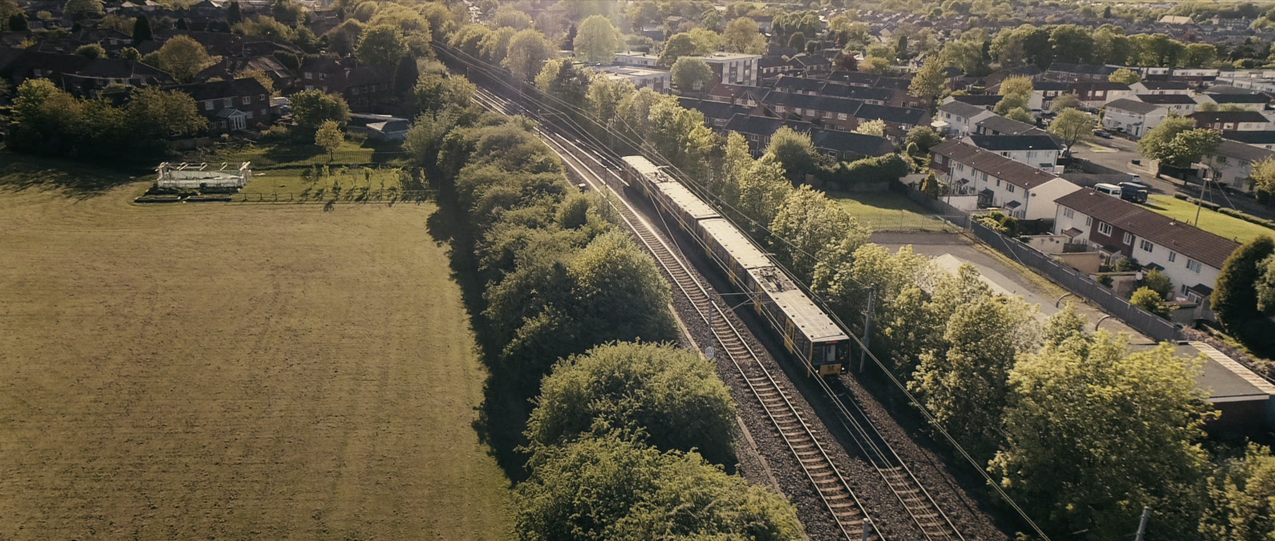 Aerial view of Tyne and Wear Metro train passing through green suburbs on a sunny day, from campaign by STORO