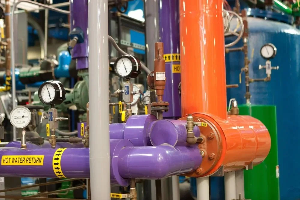 Industrial process piping and mechanical system infrastructure featuring insulated hot water return lines, pressure gauges, and commercial facility equipment designed for efficient system performance and temperature control.