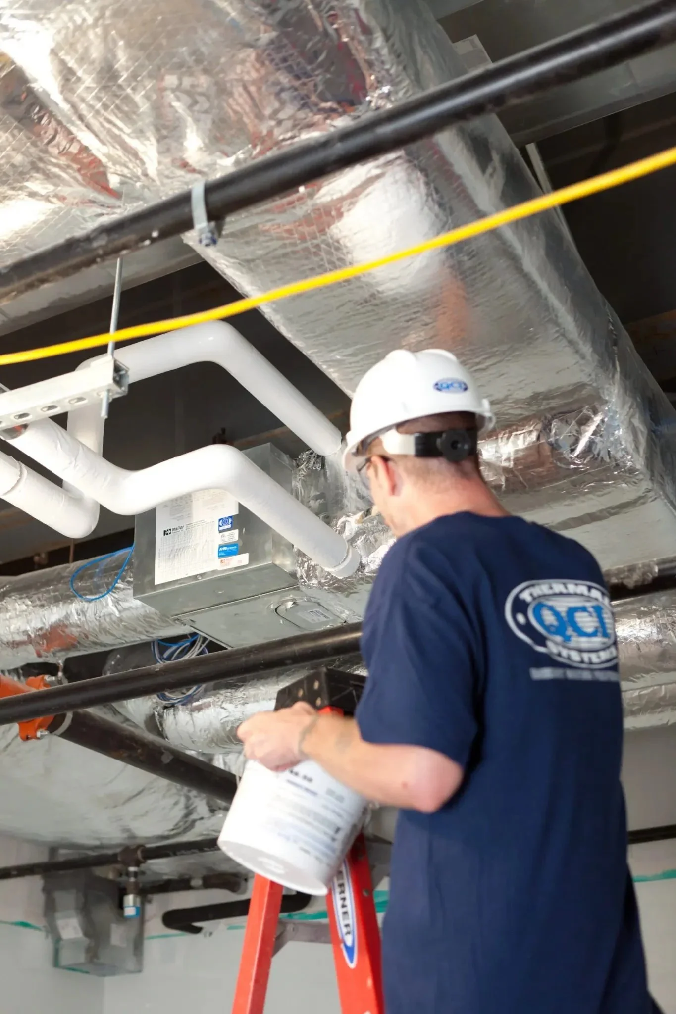 QCI Thermal Systems installer working on HVAC ductwork and mechanical insulation installation inside a commercial facility.