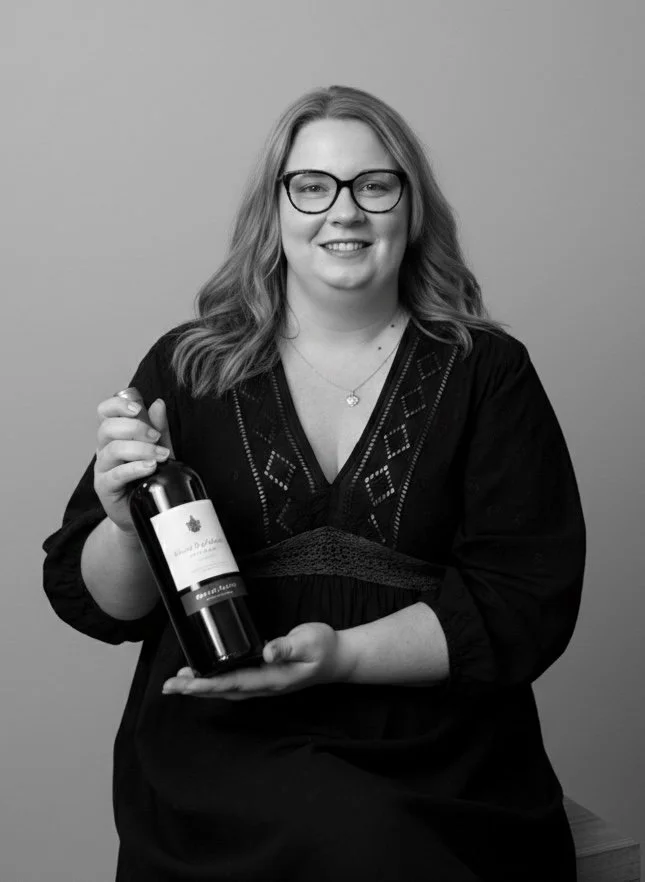 Femme souriante portant des lunettes, tenant une bouteille de vin