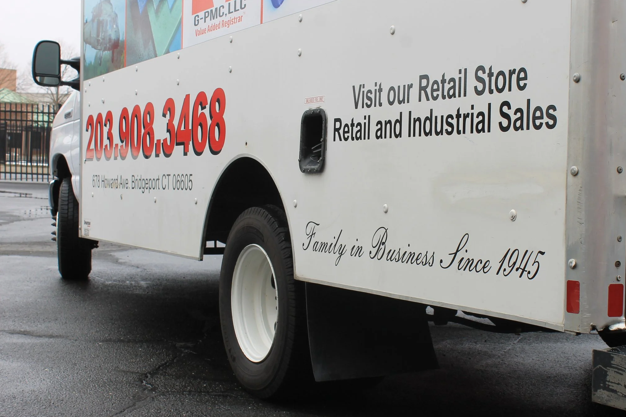 A white delivery truck with red and black lettering on the side advertising a retail store and industrial sales, plus contact information and a slogan about the family's business since 1945.