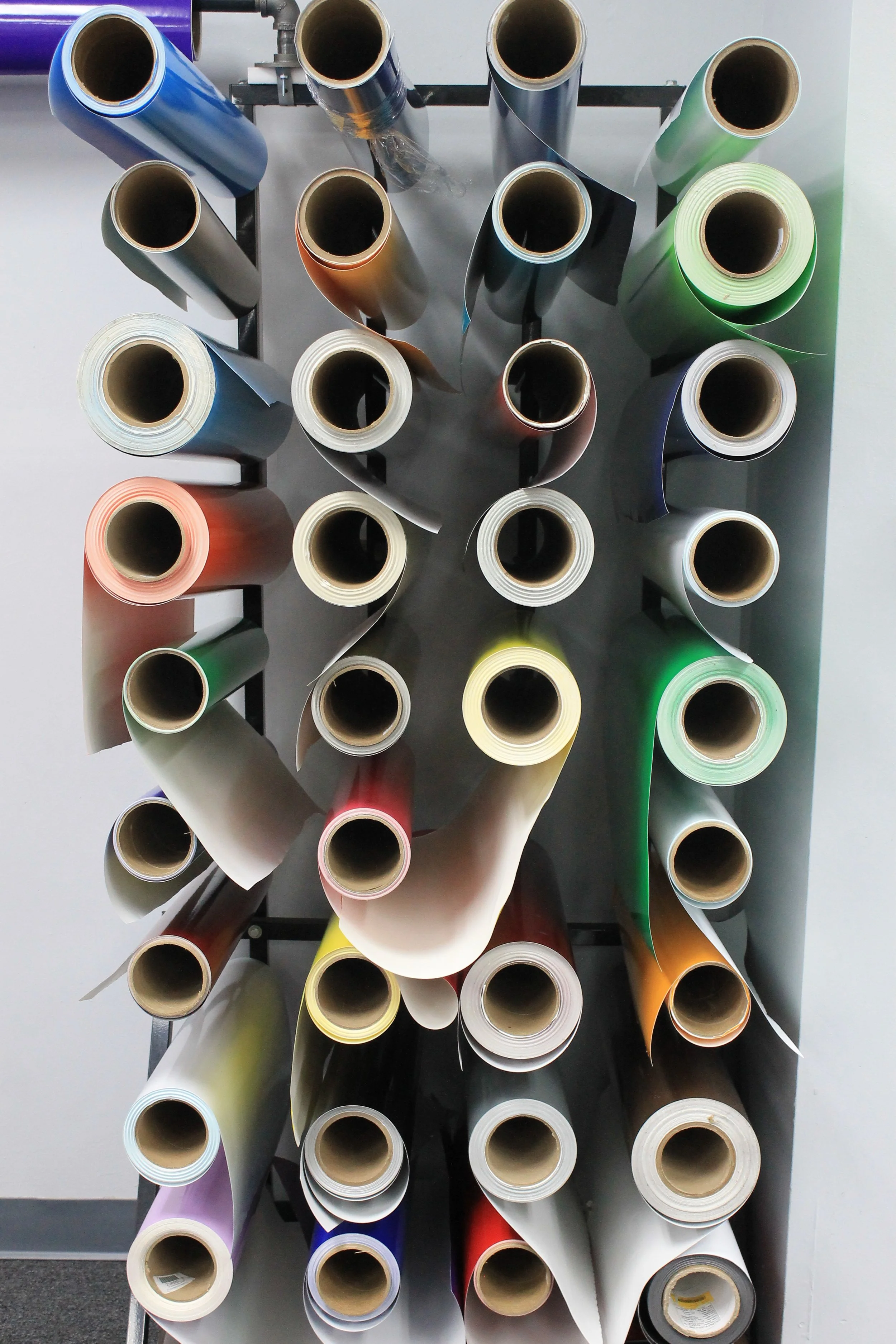 Multiple rolls of colored vinyl or paper on a rack, viewed from above.