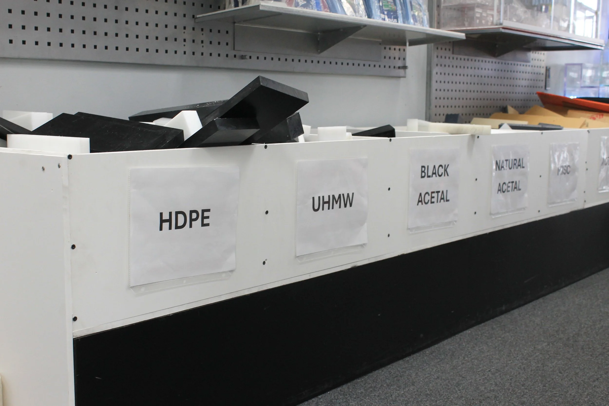 Shelving unit with different types of plastics labeled HDPE, UHMW, black acetal, natural acetal, and others.