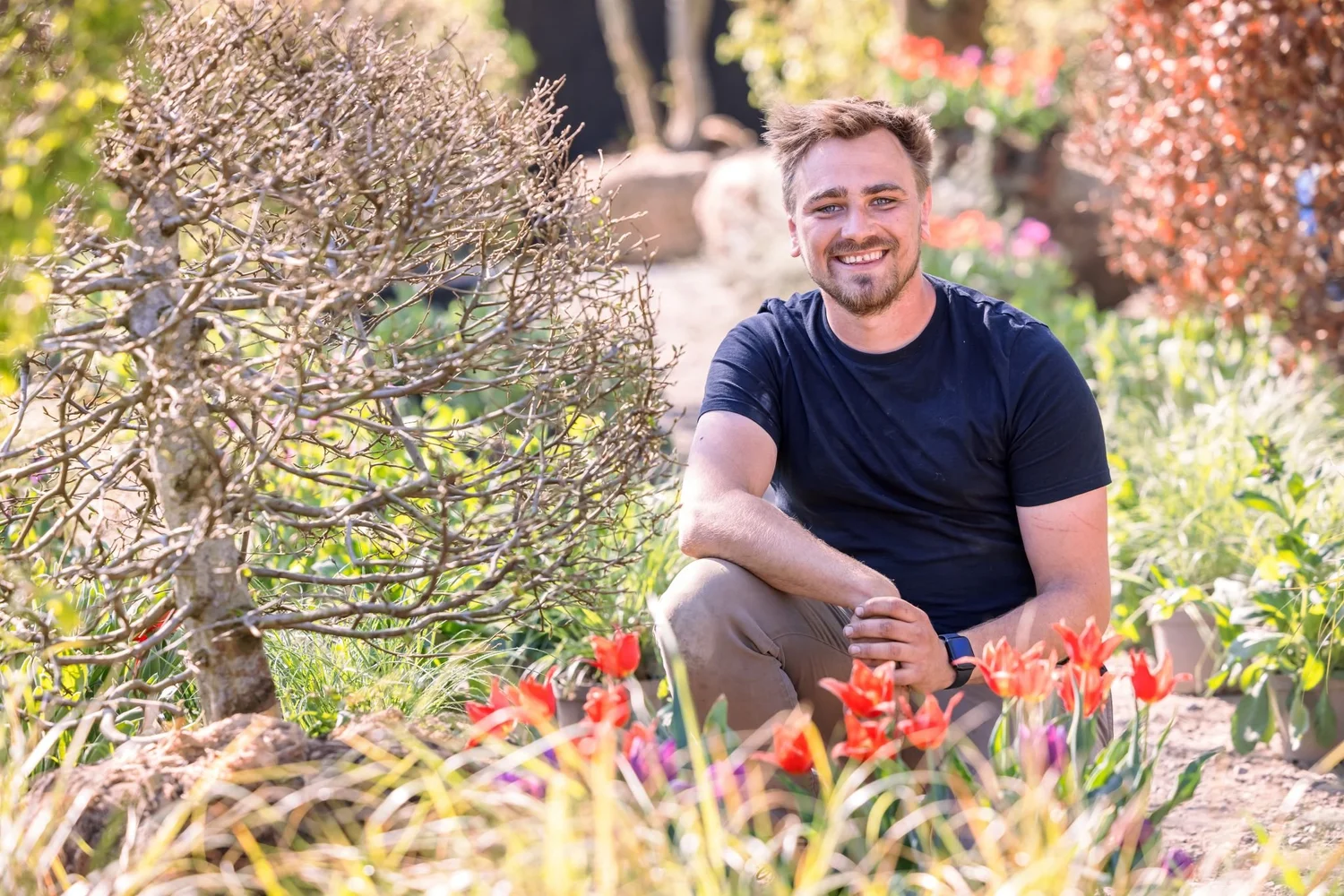 Jamie Butterworth crouching beside red tulips in a garden