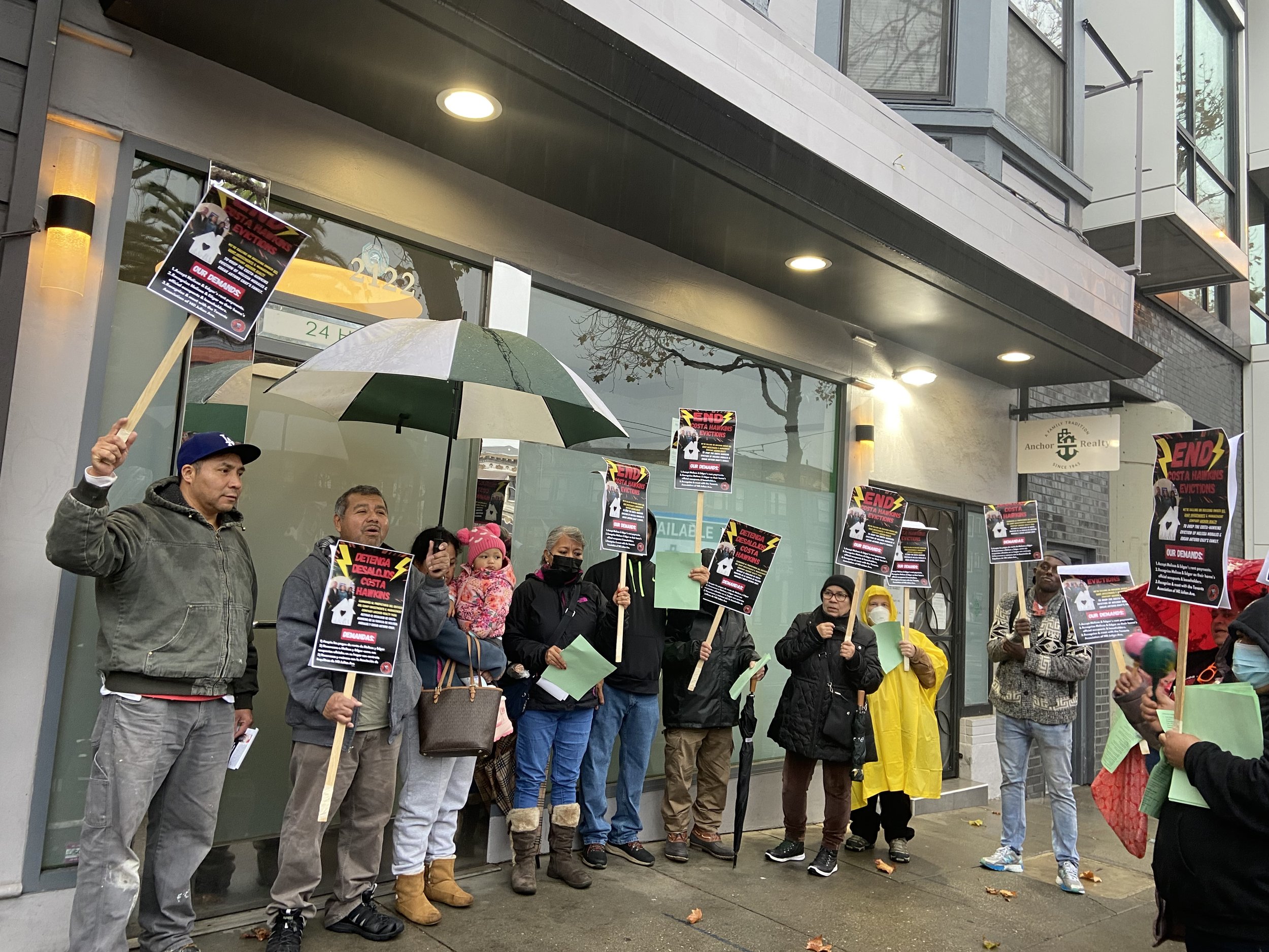 A scenic landscape featuring a large body of turquoise water in the foreground, green hills on either side, and a mountain range with rugged peaks in the background under a cloudy sky.