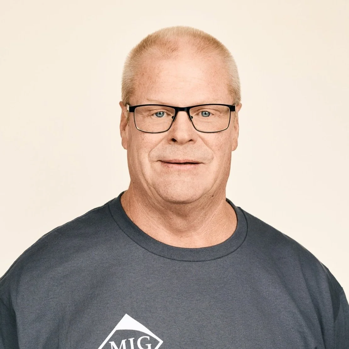 Man with glasses wearing a dark gray shirt, against a neutral background.