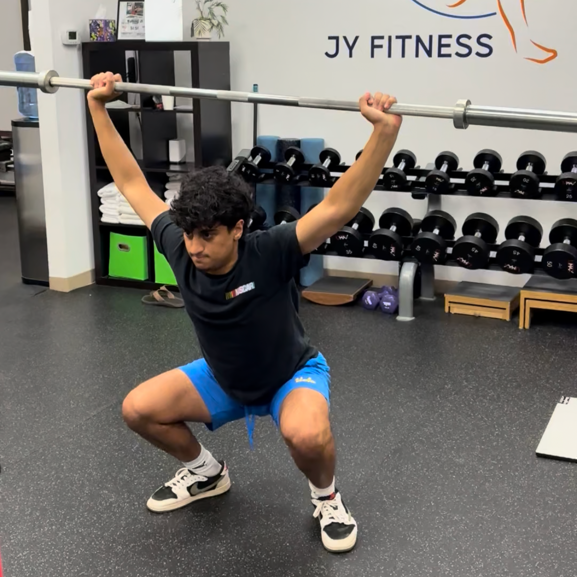Teen athlete performing an over head barbell squat with good technique in a studio gym.