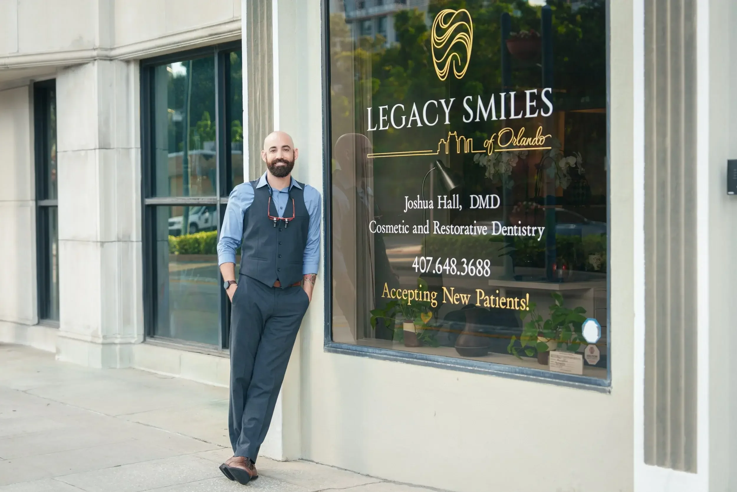 A man in a vest standing outside Legacy Smiles of Orlando, a cosmetic and restorative dentistry office, with the clinic's window displaying contact information and a notice that new patients are welcome.
