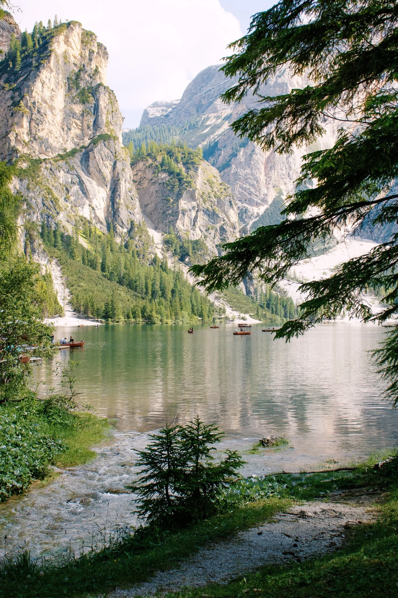 Scenic mountain lake with boats, surrounded by rocky cliffs and evergreen trees.